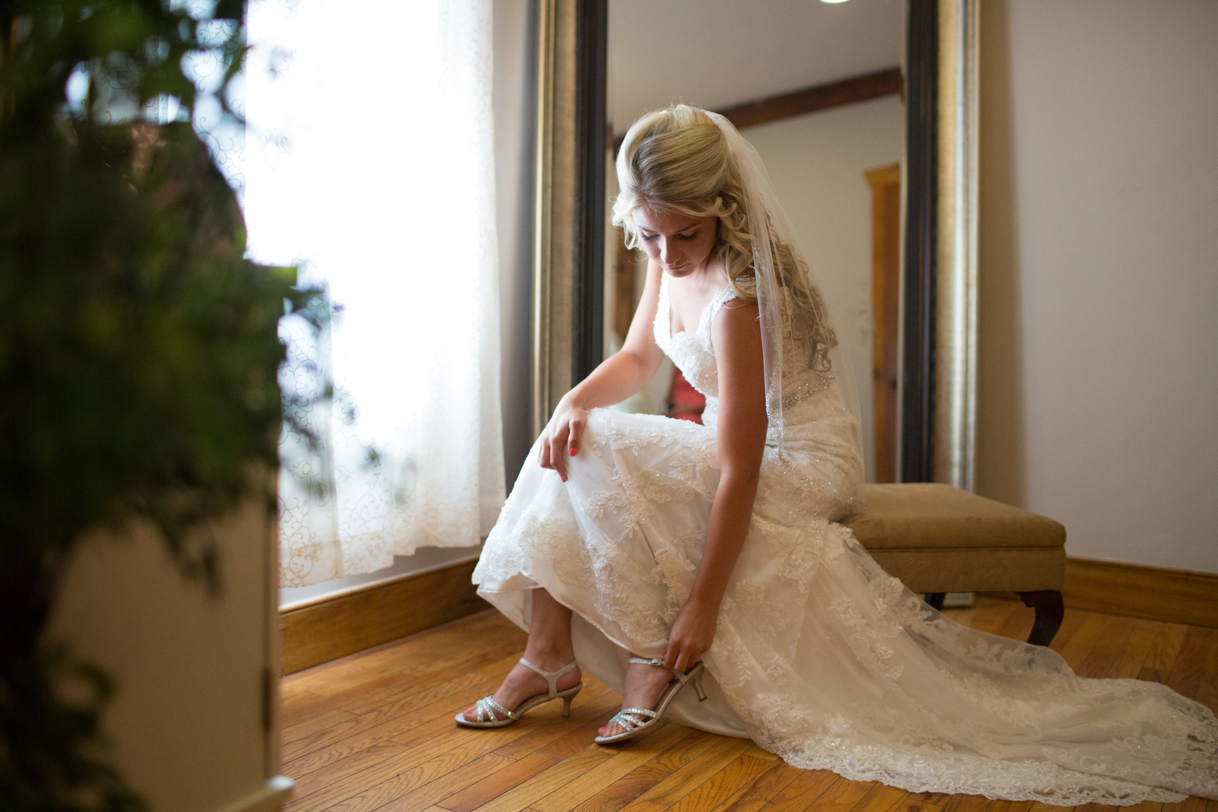 Bride putting on wedding shoes by window