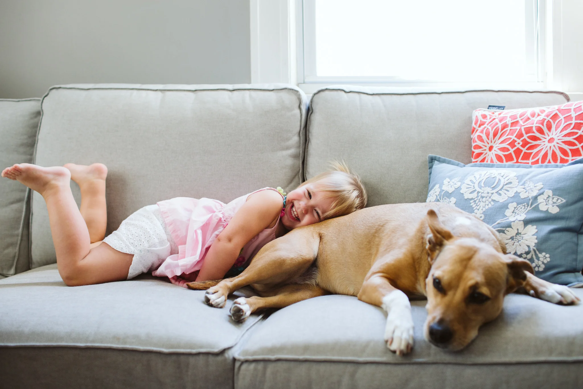 Little girl laughing on couch with dog lifestyle family session