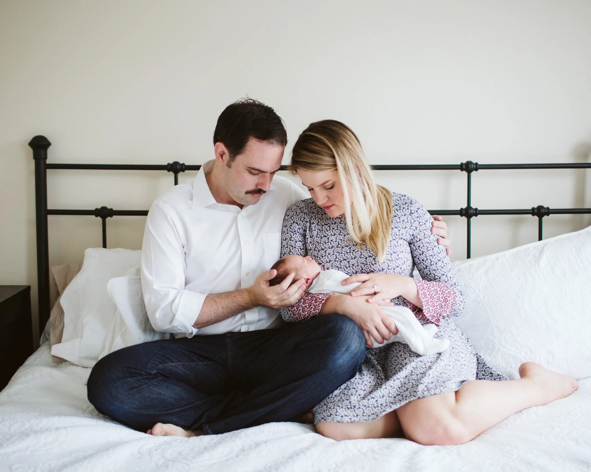 Couple holding baby on white bed during lifestyle family session