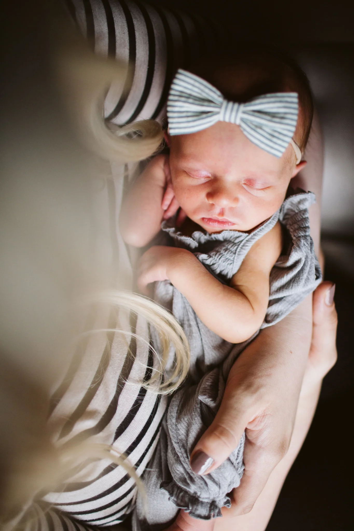 Baby with bow on head in mom's arms at home family photography session