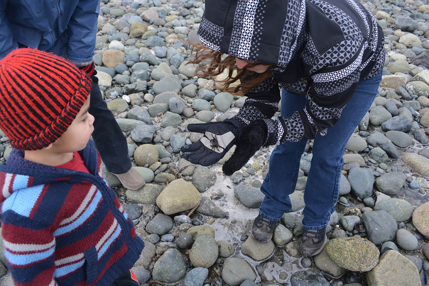 A little boy looks at a crab in a woman's hands.
