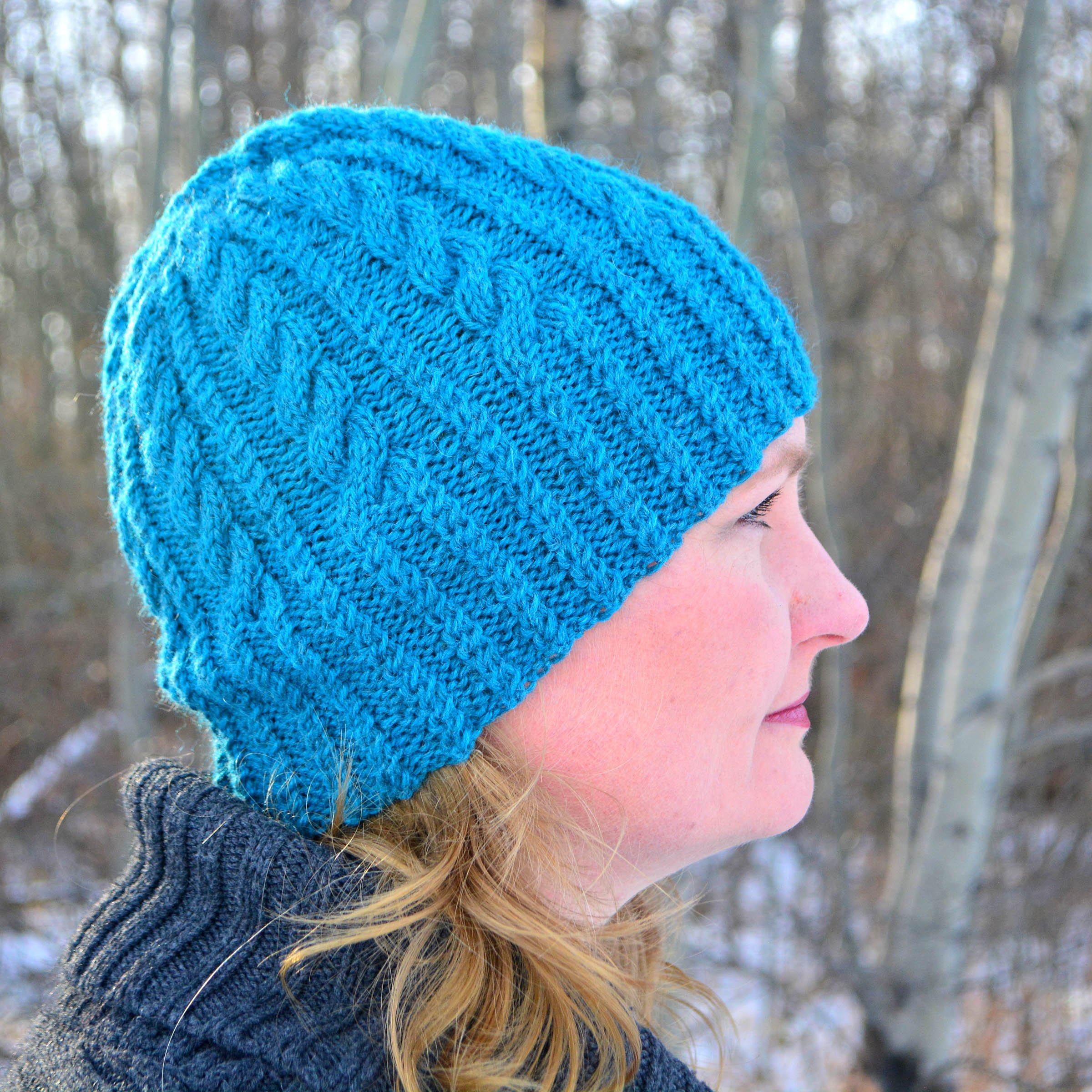 Talena in profile wearing a blue cable-knit hat in front of snowy trees