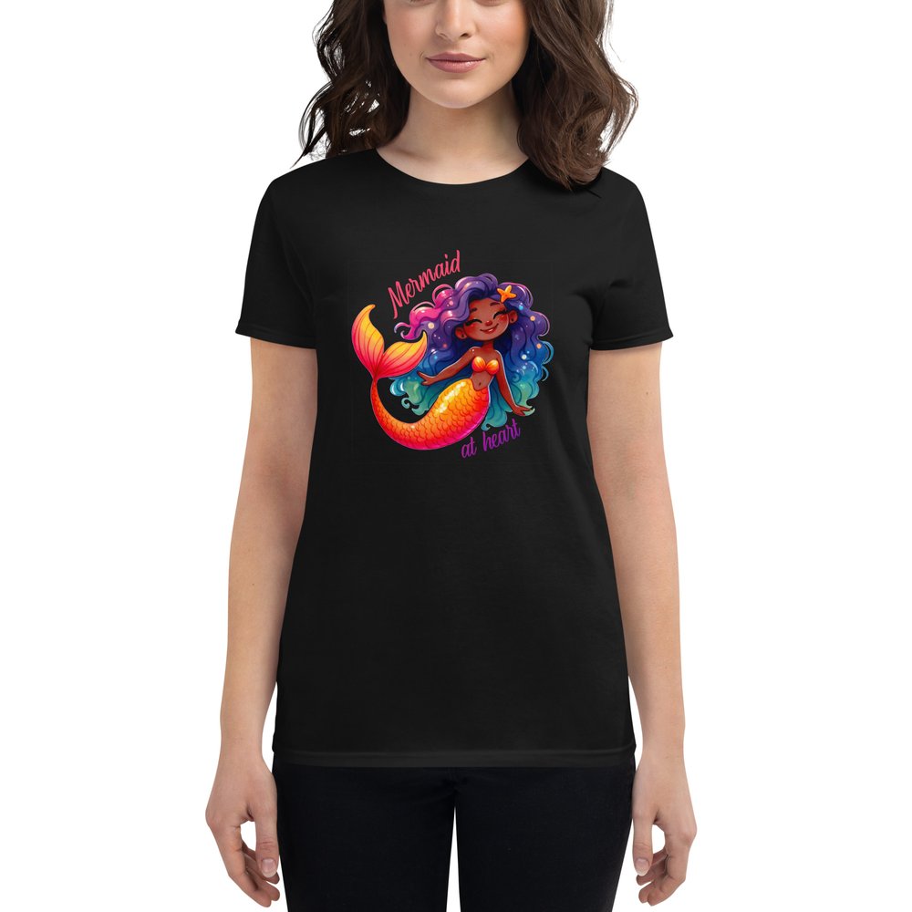 A woman in dark hair wears a black short-sleeved T-shirt with a large colourful graphic showing a sweet Black mermaid with an orange tail and long multi-coloured hair. Text: Mermaid at heart.