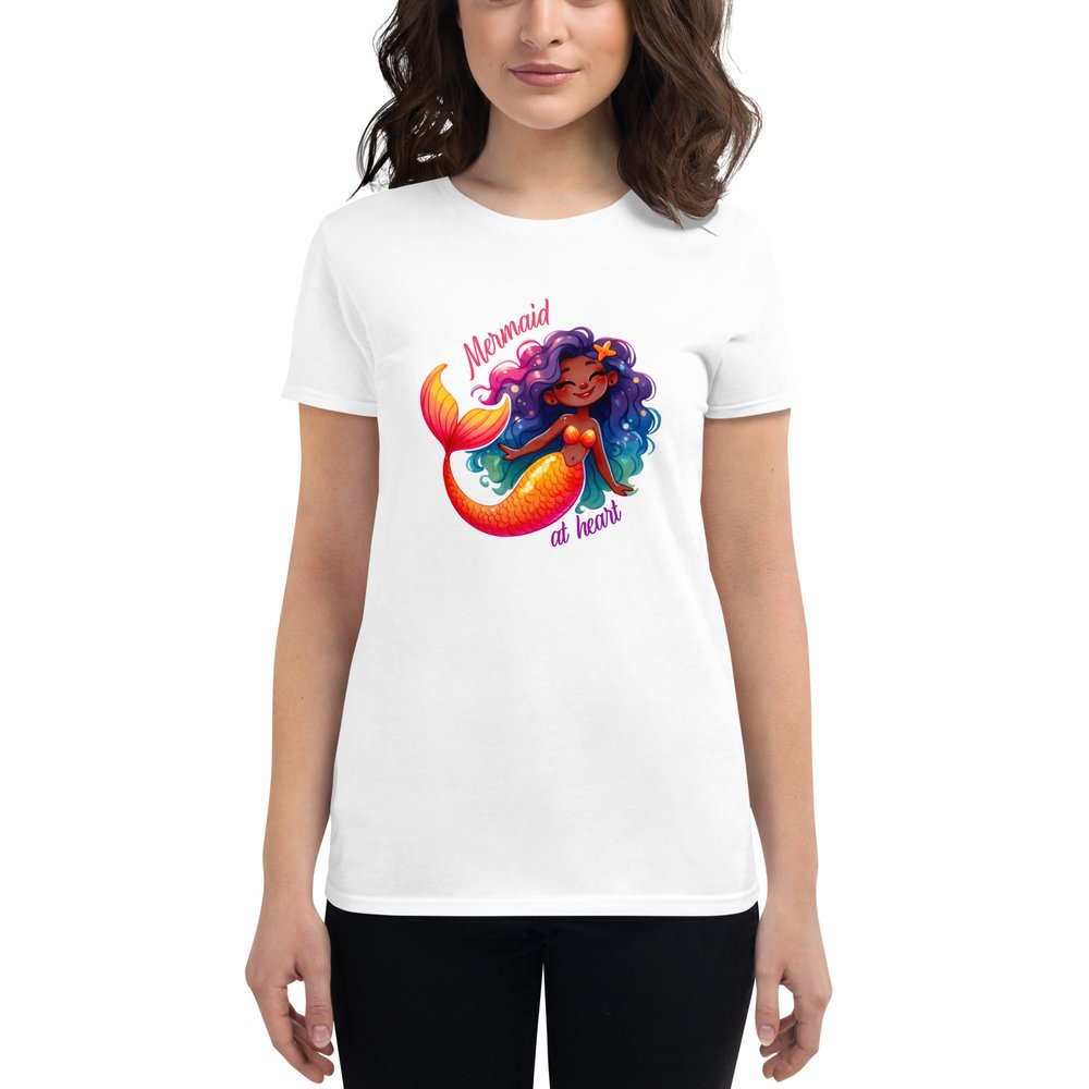 A woman in dark hair wears a white short-sleeved T-shirt with a large colourful graphic showing a sweet Black mermaid with an orange tail and long multi-coloured hair. Text: Mermaid at heart.