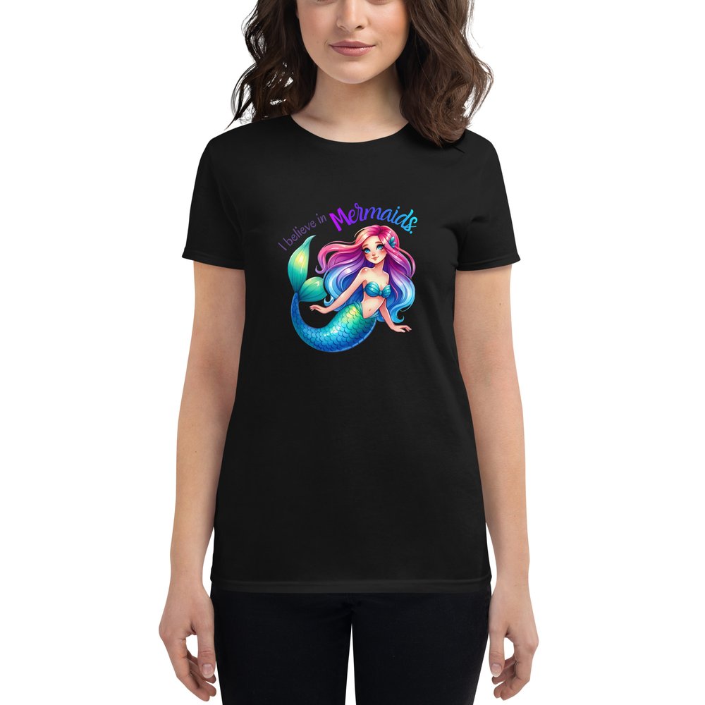 Woman wearing a black short-sleeved T-shirt with a large centered graphic of a Caucasian mermaid with rainbow hair, clam shell bra, and a blue-green tail. Text: I believe in mermaids.