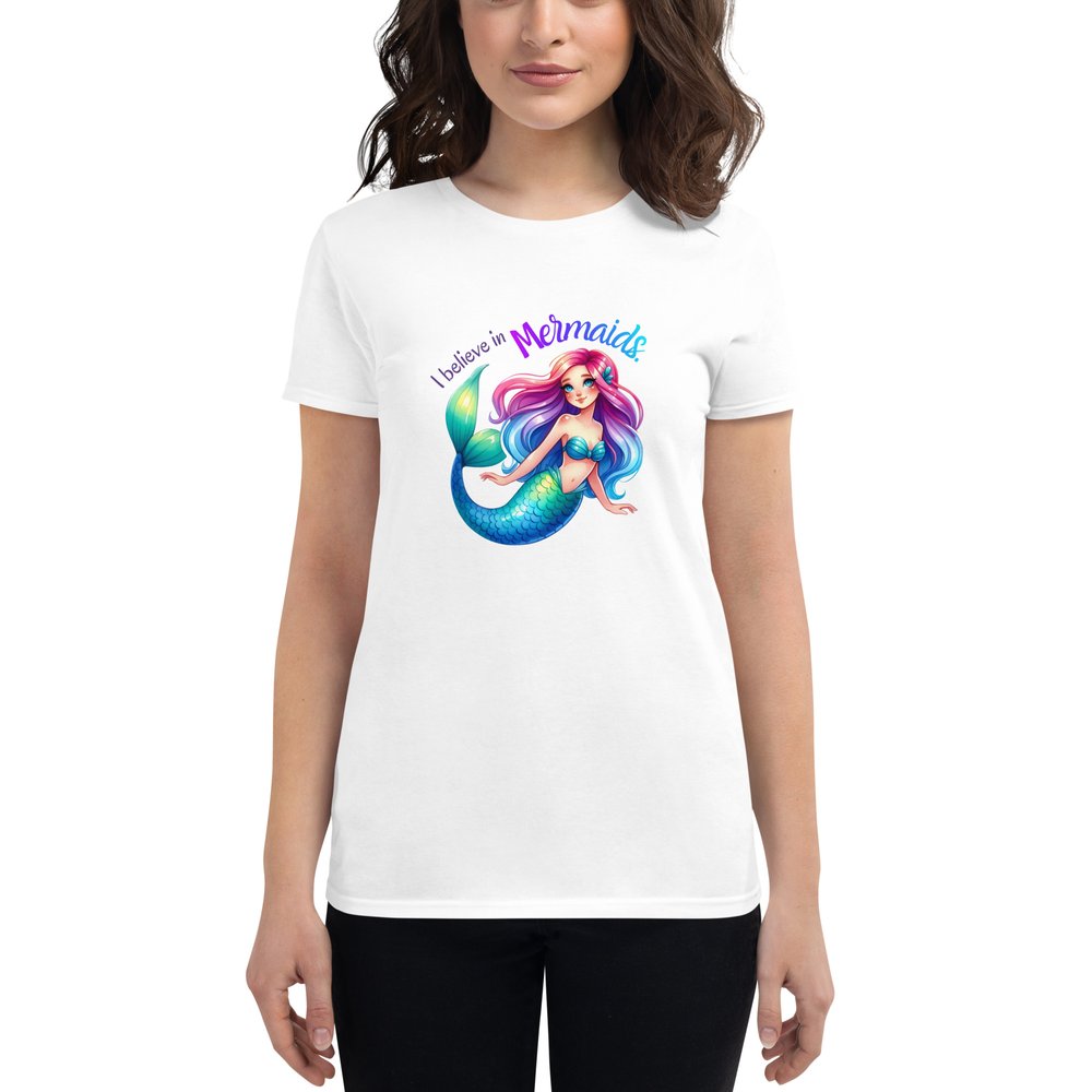 Woman wearing a white short-sleeved T-shirt with a large centered graphic of a Caucasian mermaid with rainbow hair, clam shell bra, and a blue-green tail. Text: I believe in mermaids.