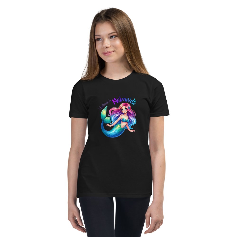 White pre-teen girl wears a black youth tee with a colourful mermaid graphic and text that reads "I believe in mermaids."