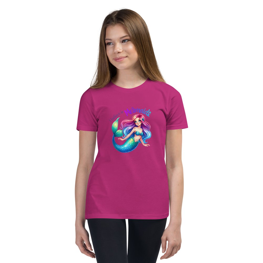 White pre-teen girl wears a berry youth tee with a colourful mermaid graphic and text that reads "I believe in mermaids."