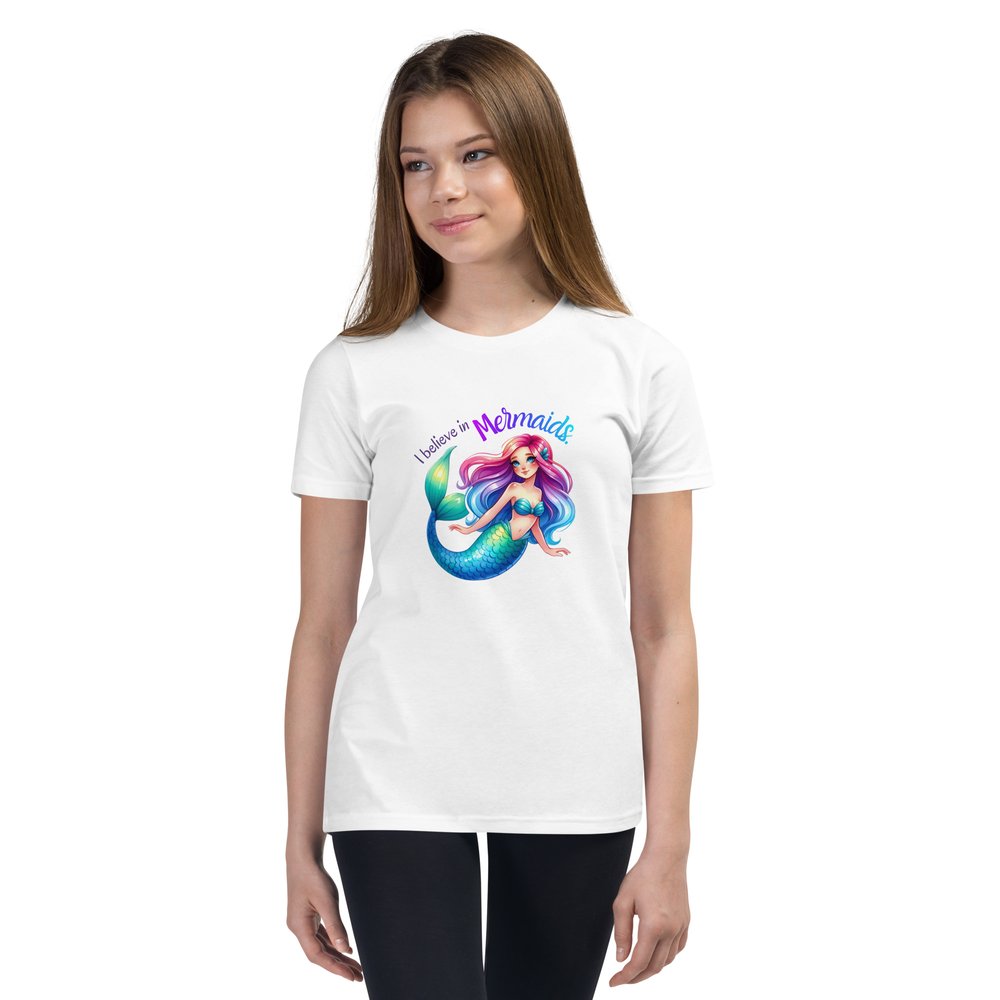 White pre-teen girl wears a white youth tee with a colourful mermaid graphic and text that reads "I believe in mermaids."