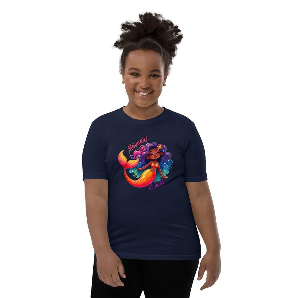 Pre-teen Black girl wearing a navy youth tee with a colourful, cute Black mermaid girl graphic and text "Mermaid at heart".