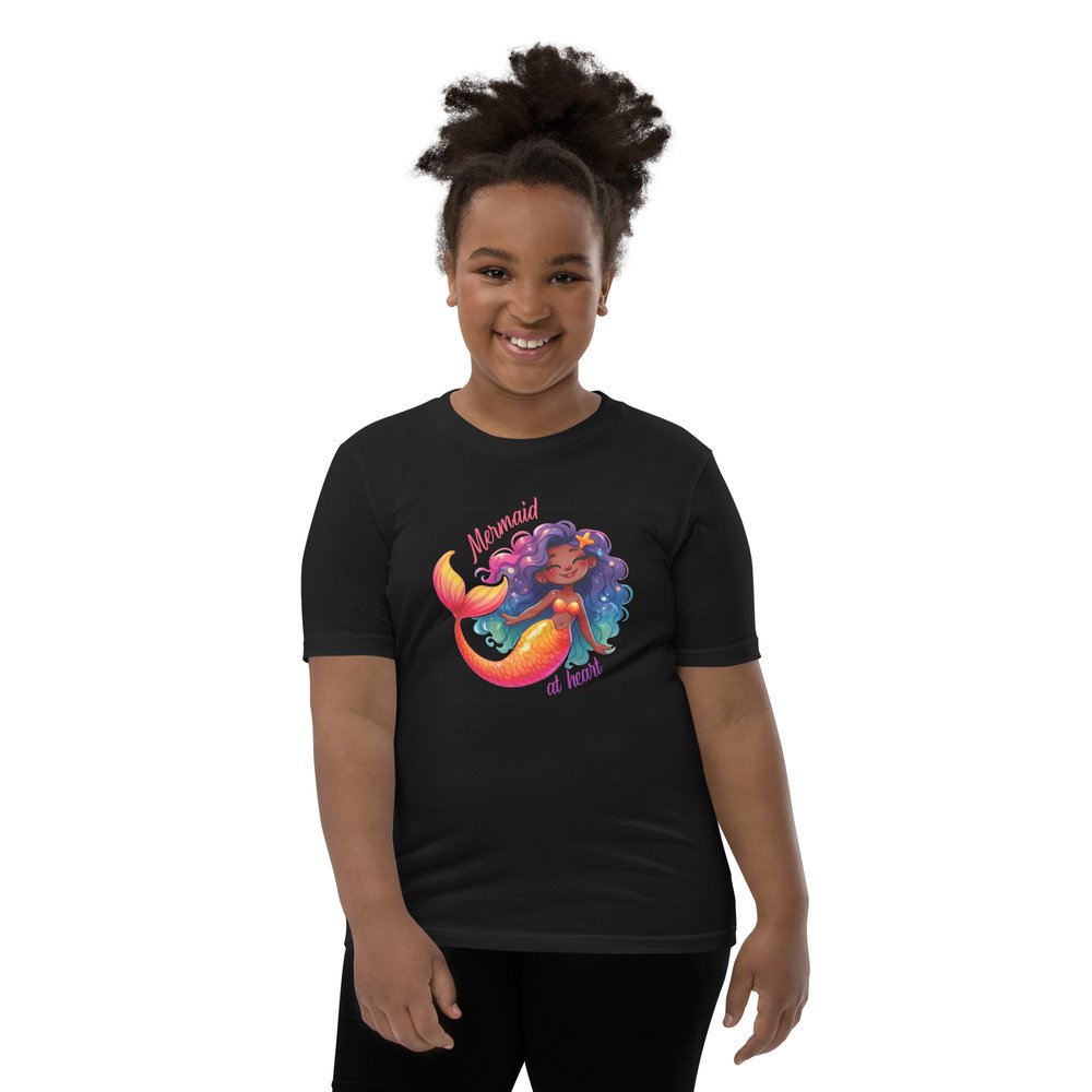 Pre-teen Black girl wearing a black youth tee with a colourful, cute Black mermaid girl graphic and text "Mermaid at heart".
