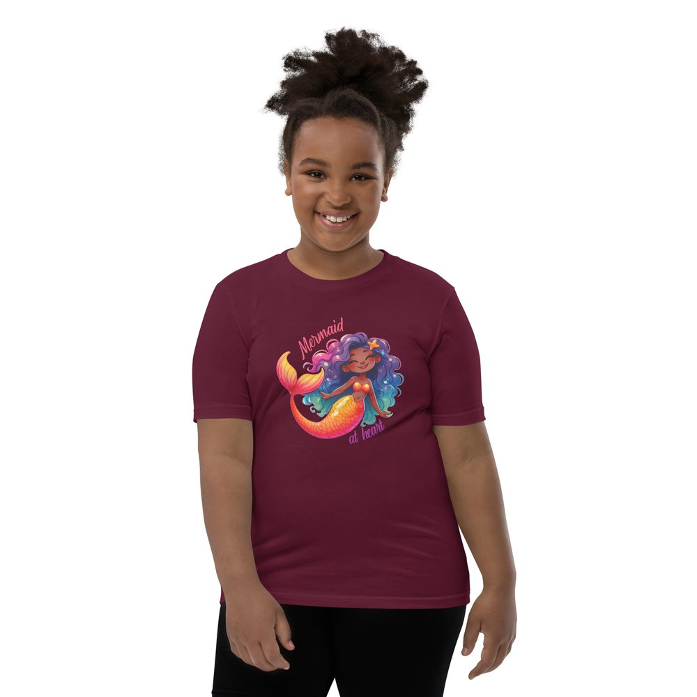 Pre-teen Black girl wearing a maroon youth tee with a colourful, cute Black mermaid girl graphic and text "Mermaid at heart".