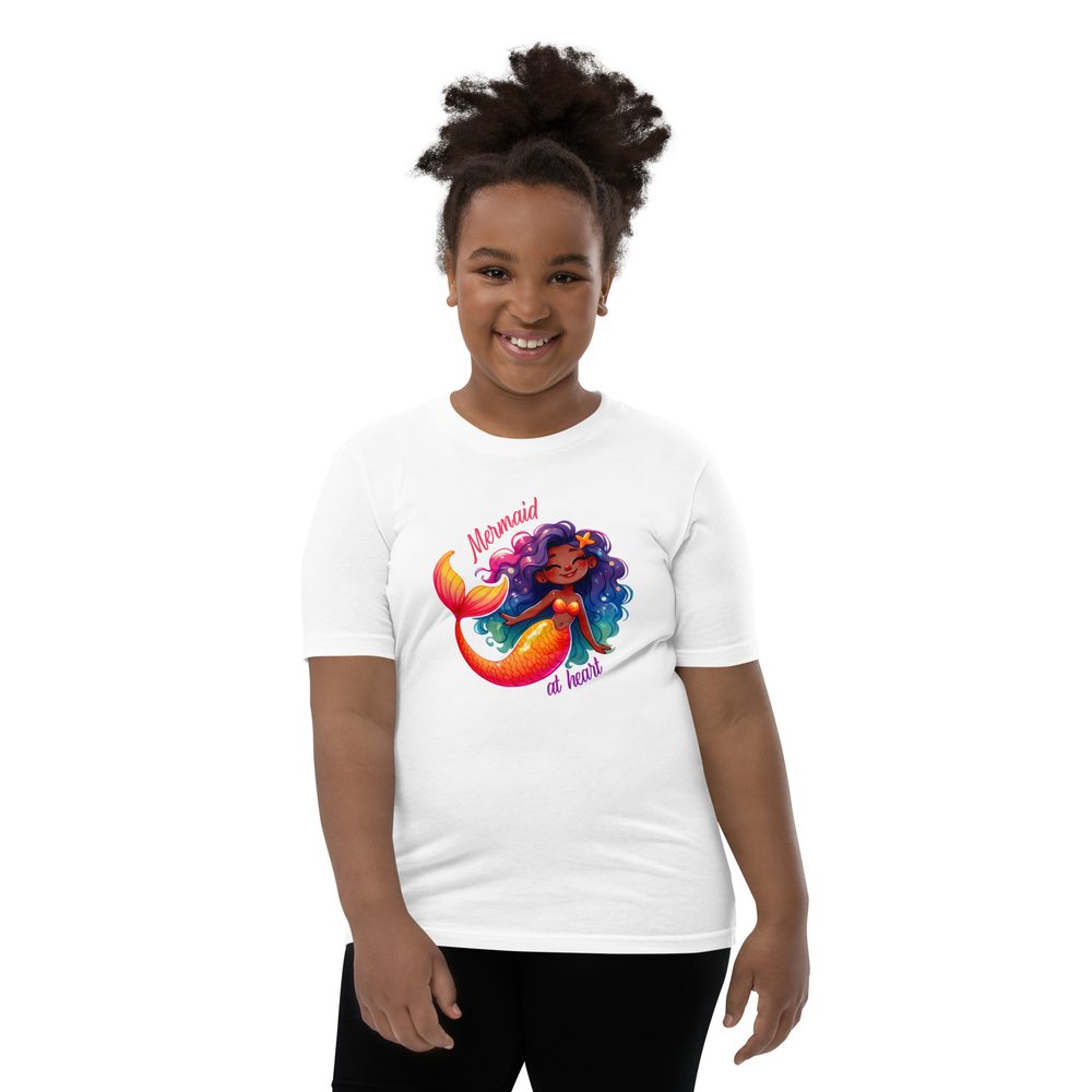 Pre-teen Black girl wearing a white youth tee with a colourful, cute Black mermaid girl graphic and text "Mermaid at heart".