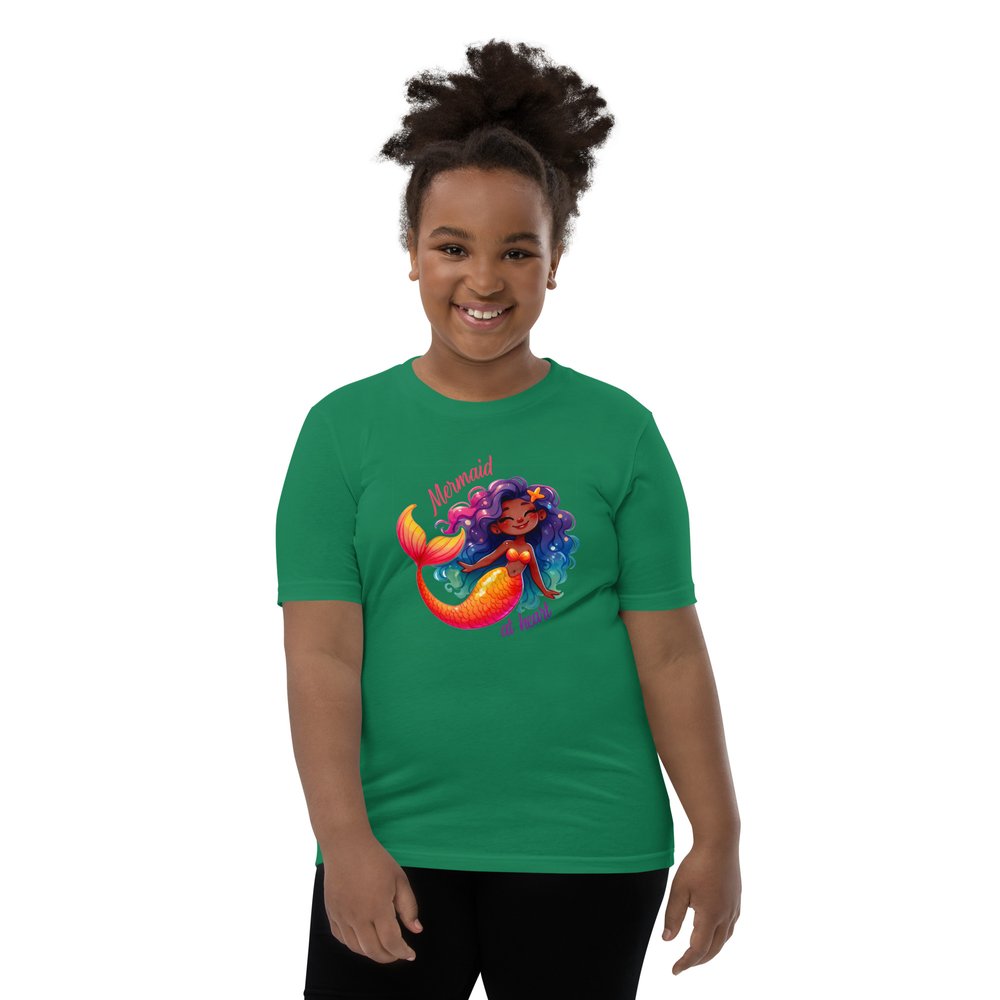 Pre-teen Black girl wearing a kelly green youth tee with a colourful, cute Black mermaid girl graphic and text "Mermaid at heart".