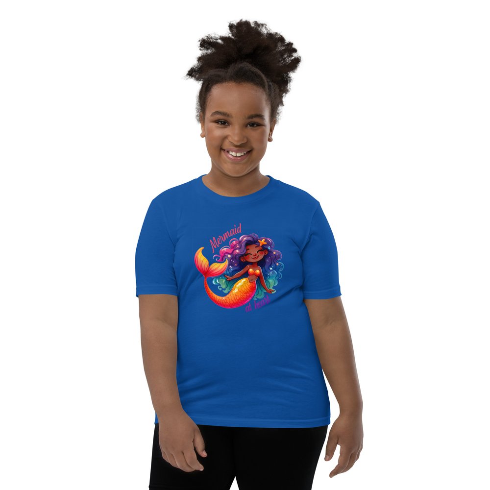 Pre-teen Black girl wearing a royal blue youth tee with a colourful, cute Black mermaid girl graphic and text "Mermaid at heart".