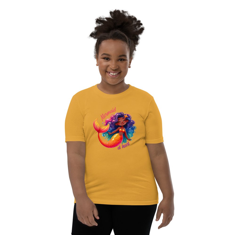 Pre-teen Black girl wearing a mustard yellow youth tee with a colourful, cute Black mermaid girl graphic and text "Mermaid at heart".