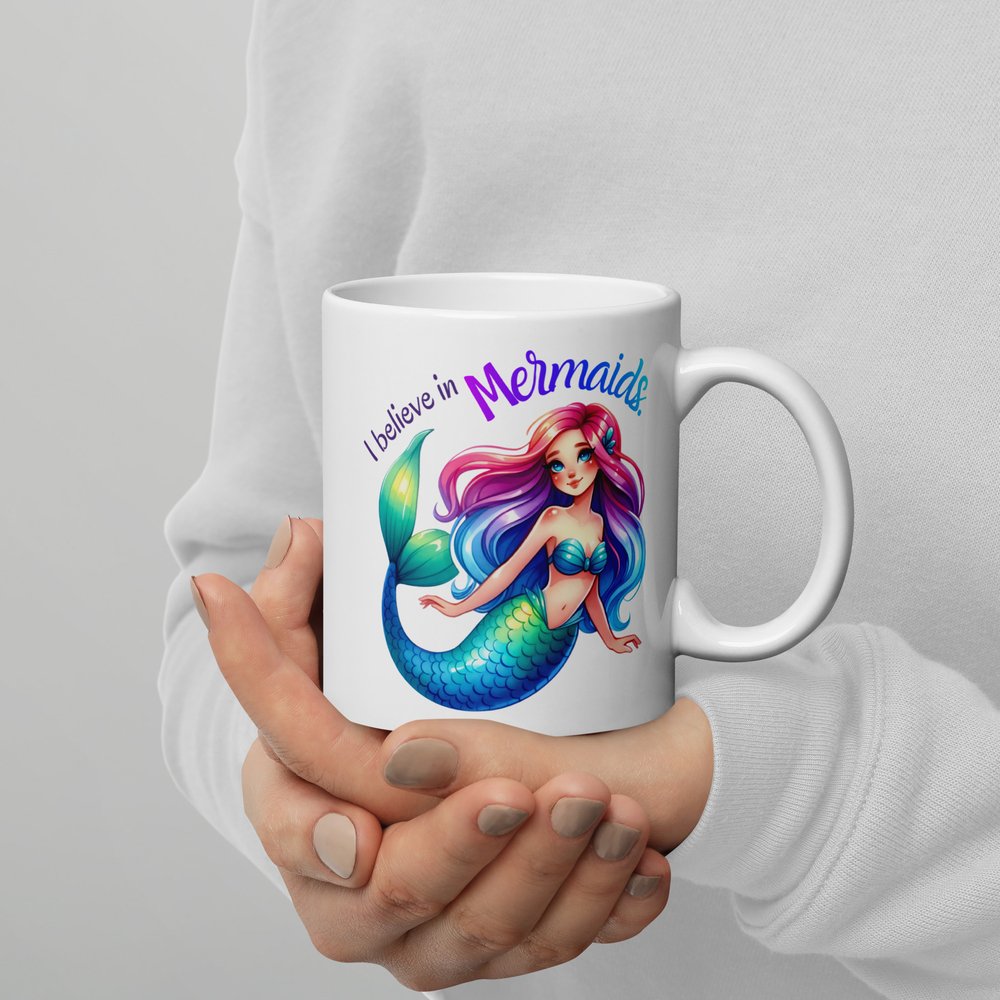 11-ounce white ceramic mug with handle on the rightshowing a colourful Caucasian mermaid graphic with text that reads "I believe in mermaids".