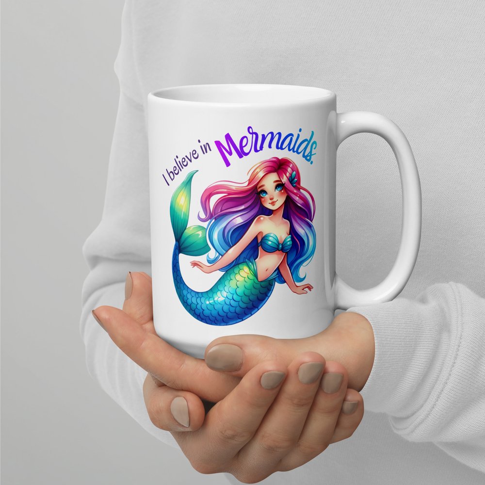 15-ounce white ceramic mug with handle on the rightshowing a colourful Caucasian mermaid graphic with text that reads "I believe in mermaids".