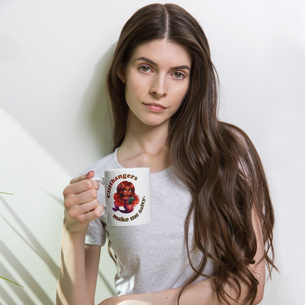 Woman holding 11-ounce white ceramic mug with a colourful, sassy brown mermaid graphic with text that reads "Cliffhangers make me salty".