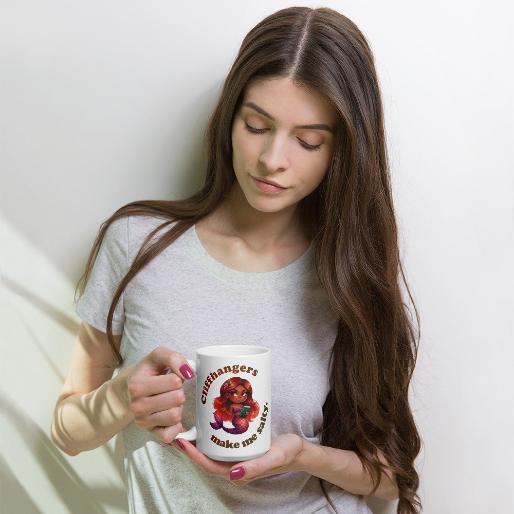 Woman holding 15-ounce white ceramic mug with a colourful, sassy brown mermaid graphic with text that reads "Cliffhangers make me salty".