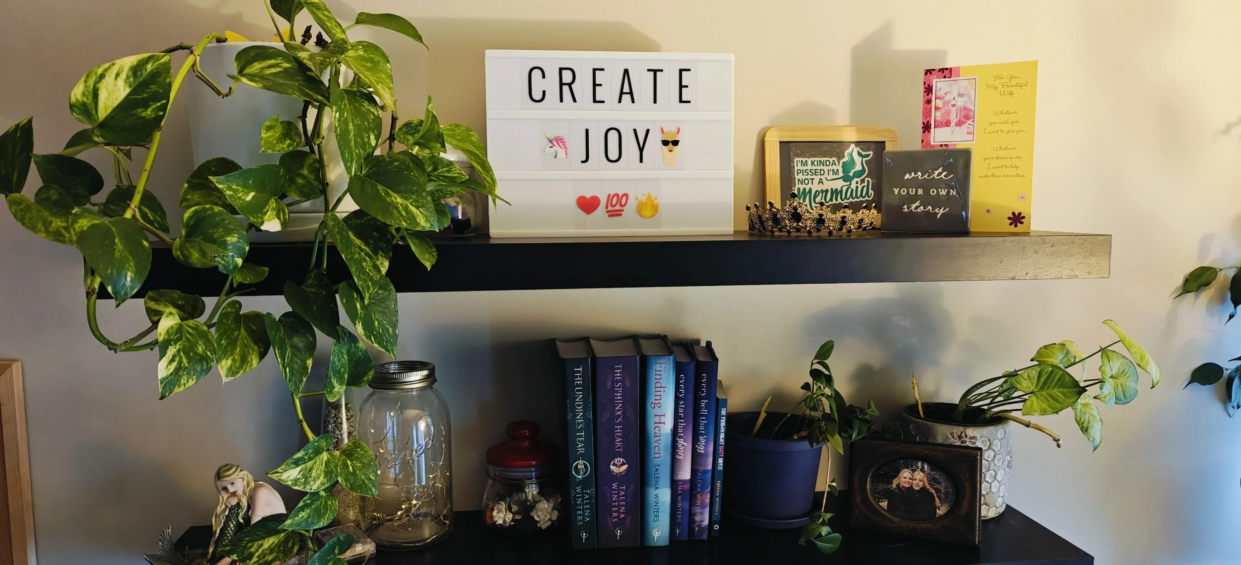 Photo of the shelves above Talena's desk with a marquis that reads "Create joy".