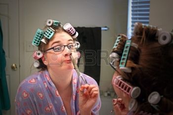 15764466-a-young-caucasian-girl-wearing-a-colorful-robe-curlers--and-glasses-makes-a-funny-face-while-she-tri.jpg