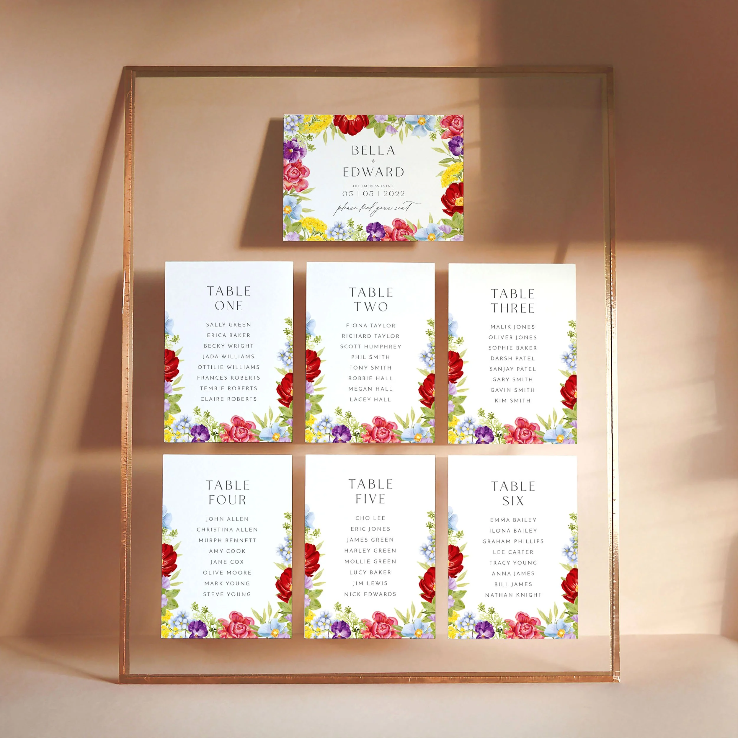 A set of small A6 printed table plan cards in a glass frame with copper edges. The design has bright watercolour florals in shades of red, pink, purple, blue, yellow and green.