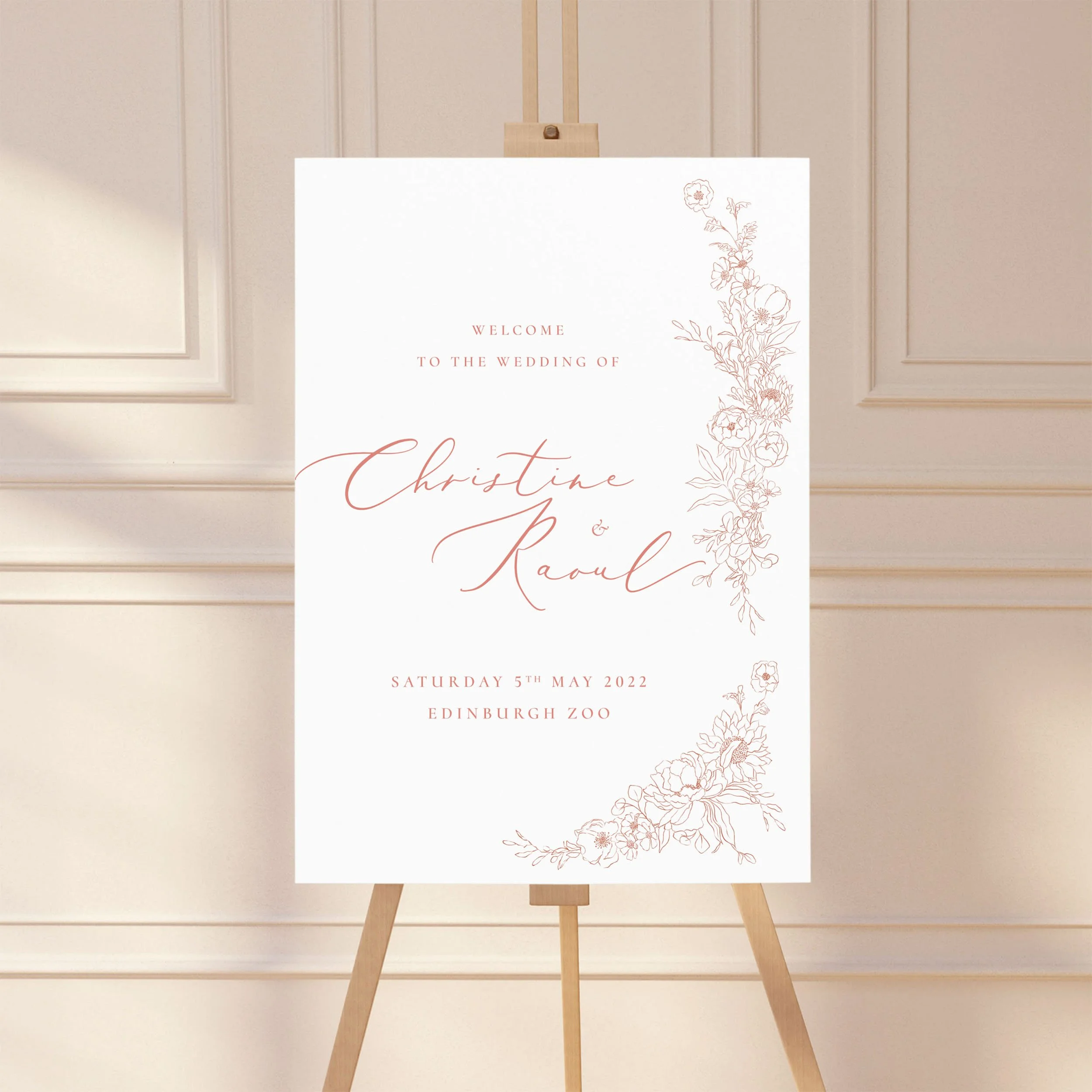 A large wedding welcome sign on an easel with a hand-drawn blush pink design.