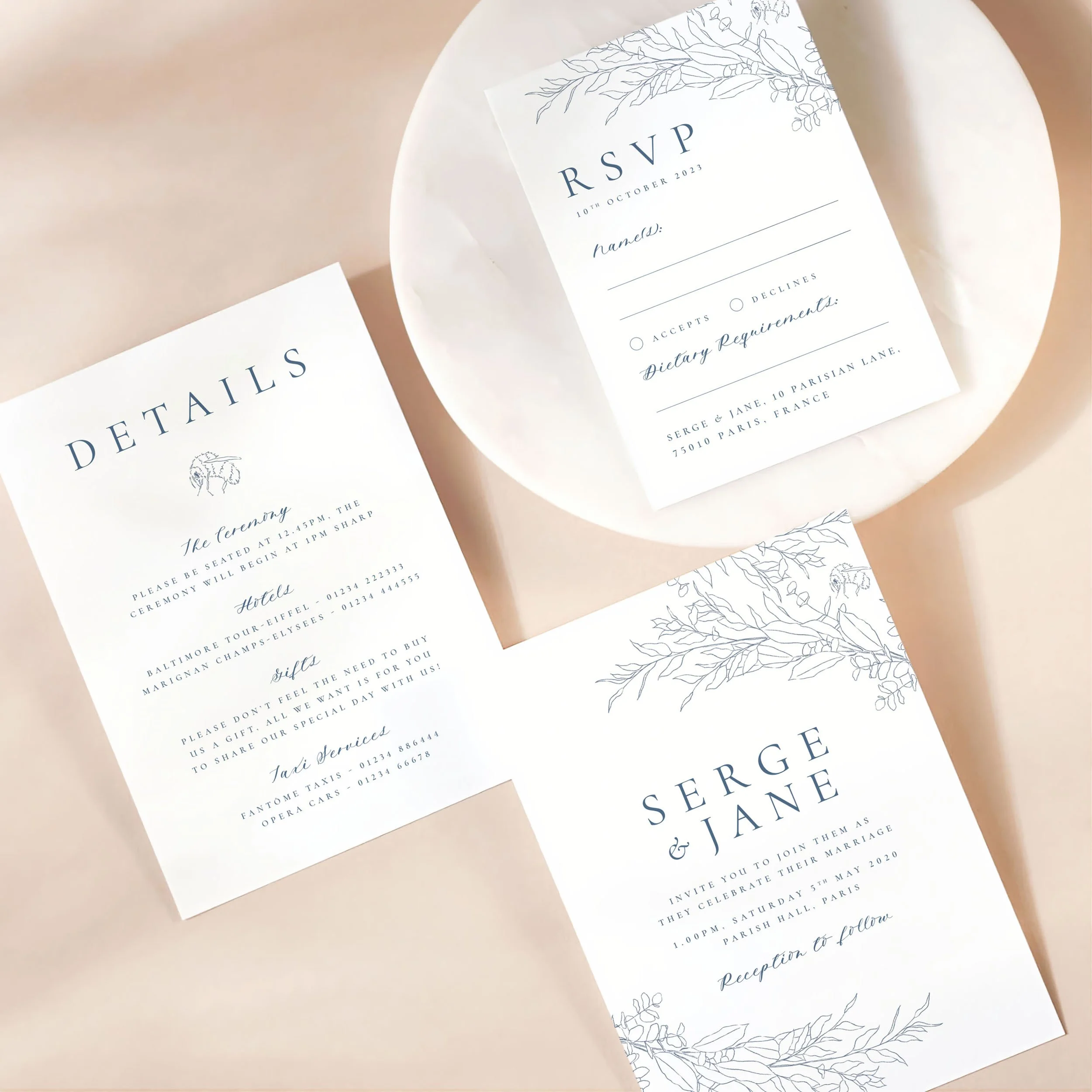 A wedding invitation card with details card and rsvp on a marble dish. There is a modern leafy motif design on each card.