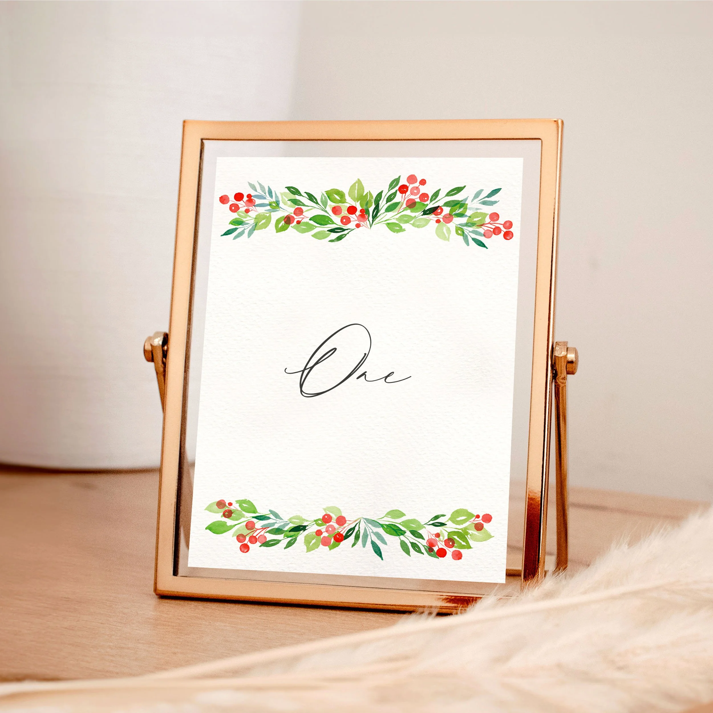 A table wedding number card in a rose gold frame with green watercolour leaves and red berries framing the top and bottom.