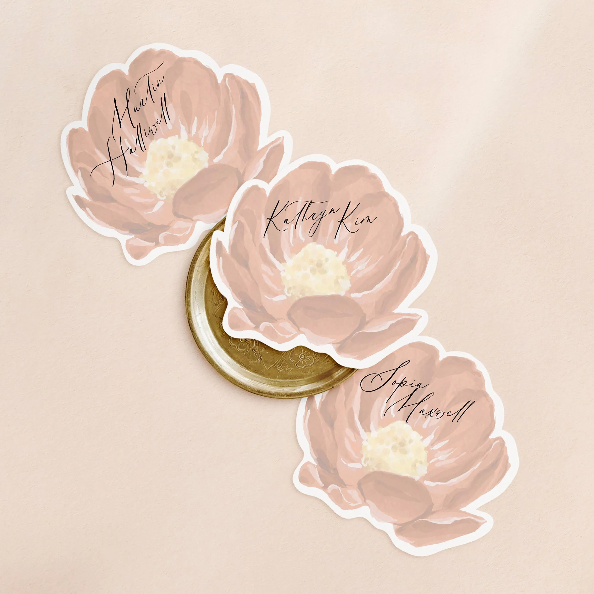 Three flower shaped wedding place cards with a faded red watercolour flower and a guest name printed on each.