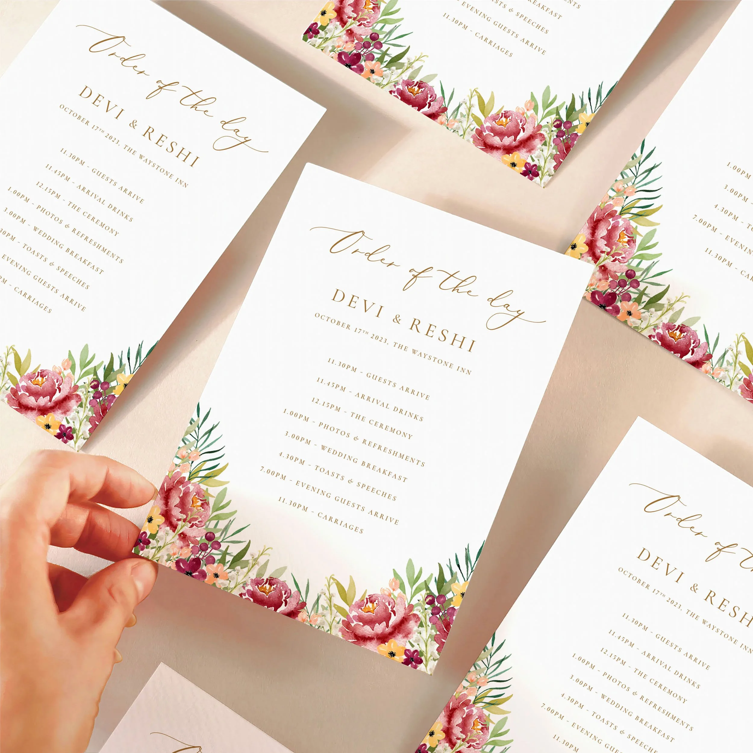 A hand picking up an order of the day timeline card with a autumnal burgundy watercolour design