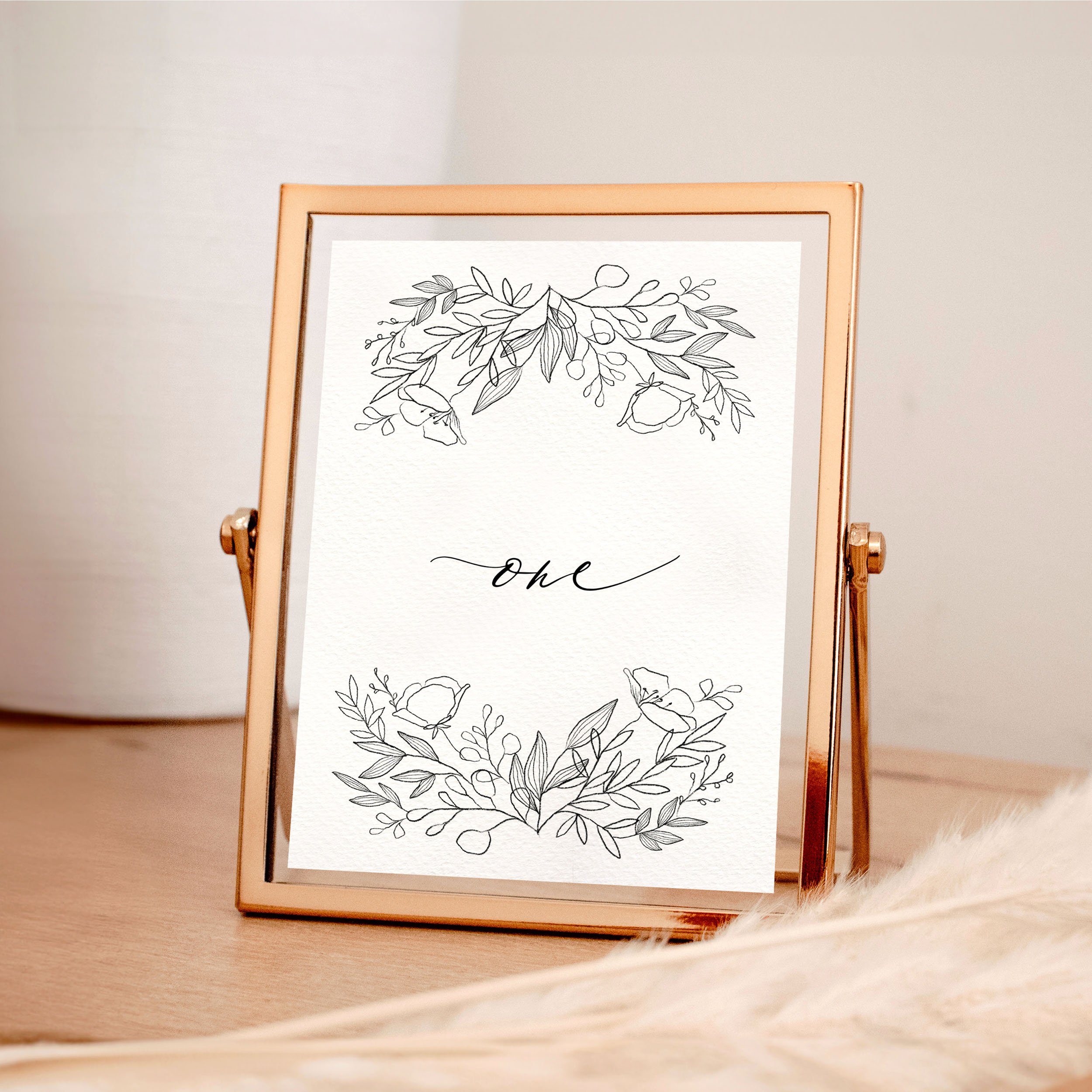 A table wedding number card in a rose gold frame with hand drawn botanical and floral elements framing the design at the top and bottom.