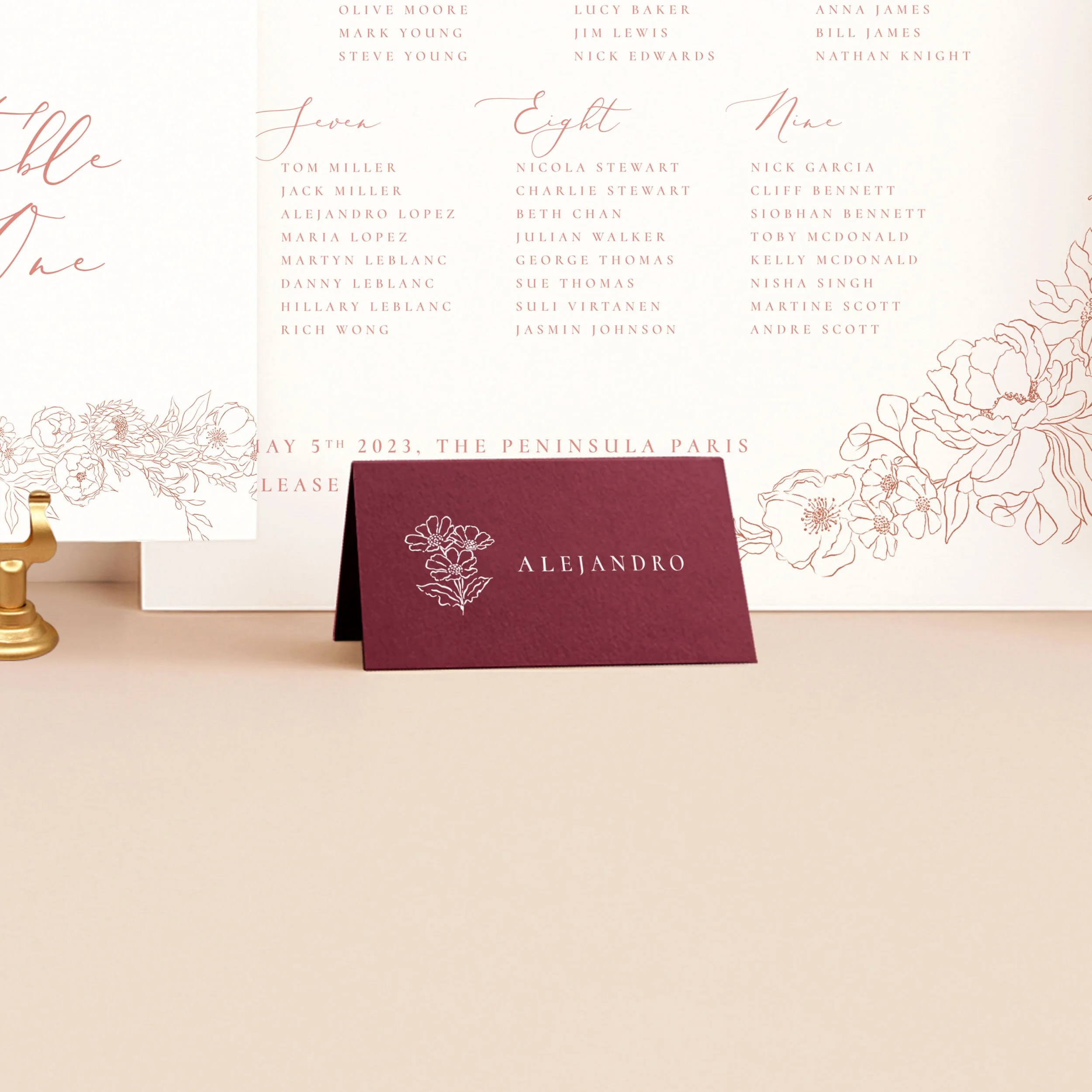 A burgundy tent place card, printed in white ink with a guest name and a small flower illustration.