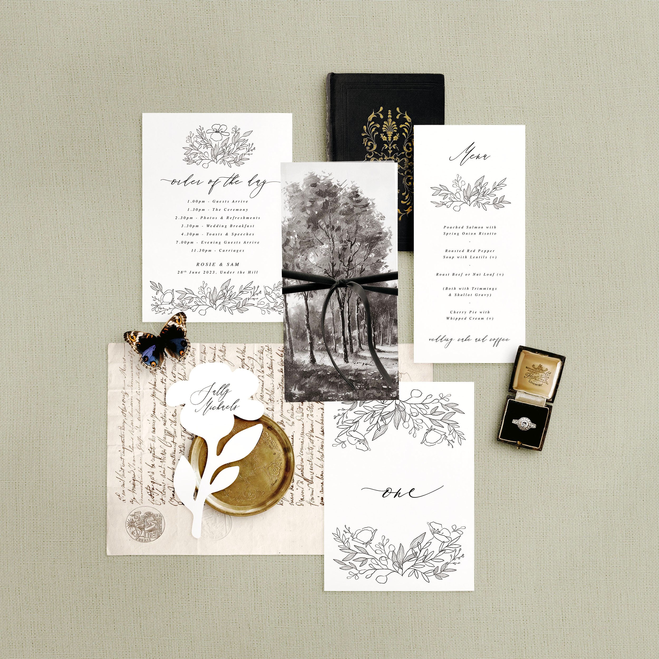 Wedding stationery flat lay featuring a menu, table number, order of the day and a flower shaped place card. A hand-drawn minimal floral design.