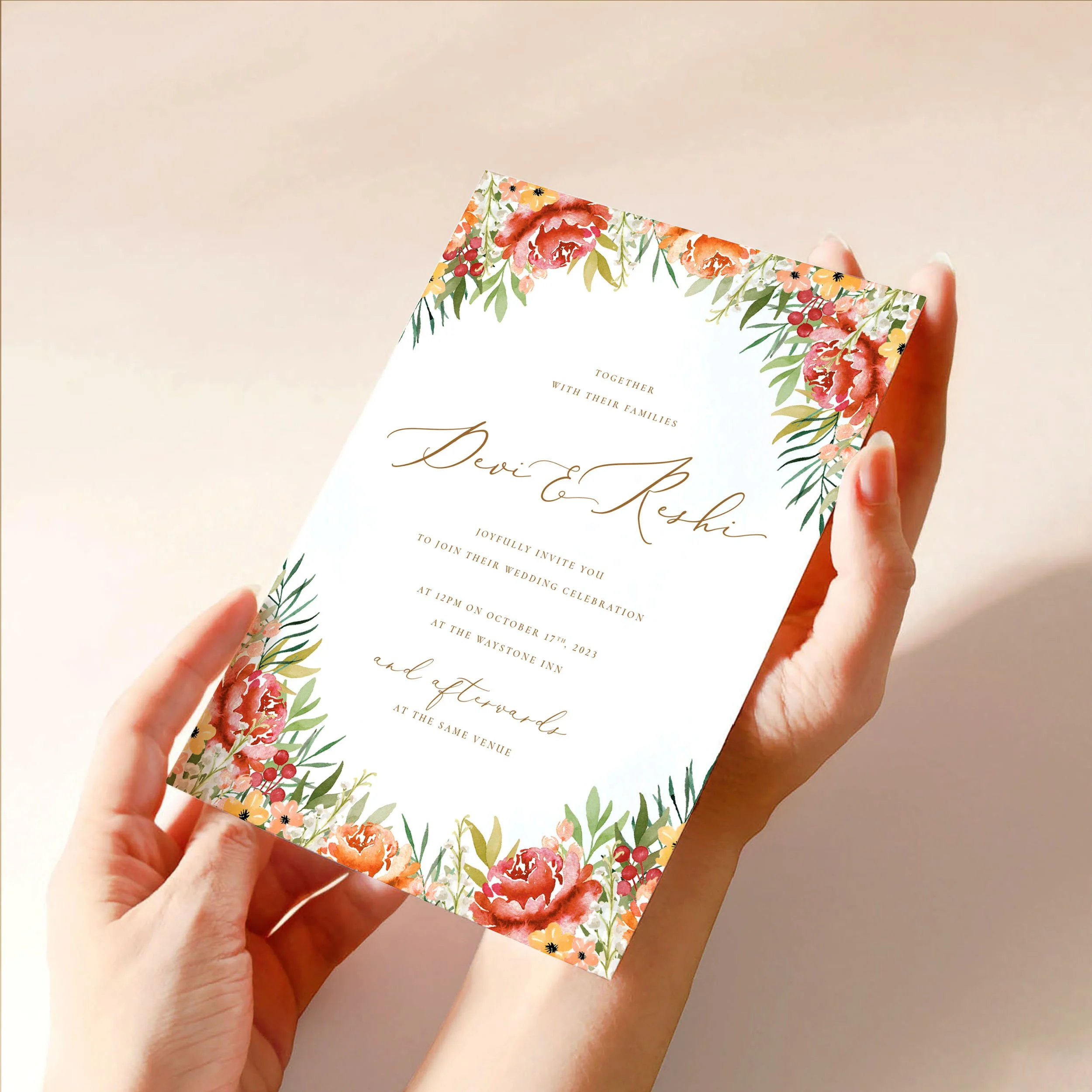 Two hands hold a 5x7" wedding invitation card. The card has a soft burnt orange and burgundy watercolour floral design with green leaves around the edges and gold text.