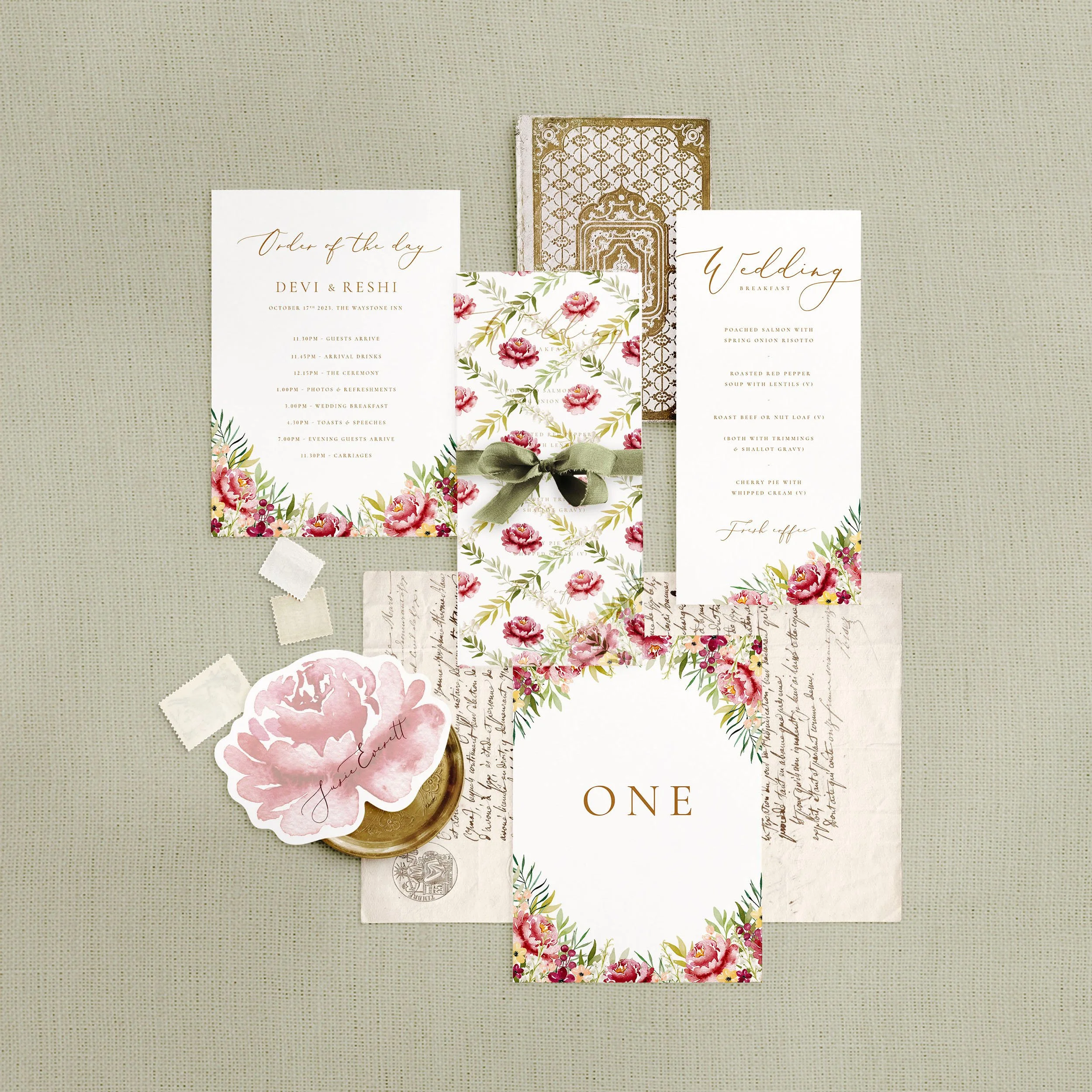 Wedding stationery flat lay featuring a menu, table number, order of the day and a flower shaped place card. A burgundy watercolour floral design.