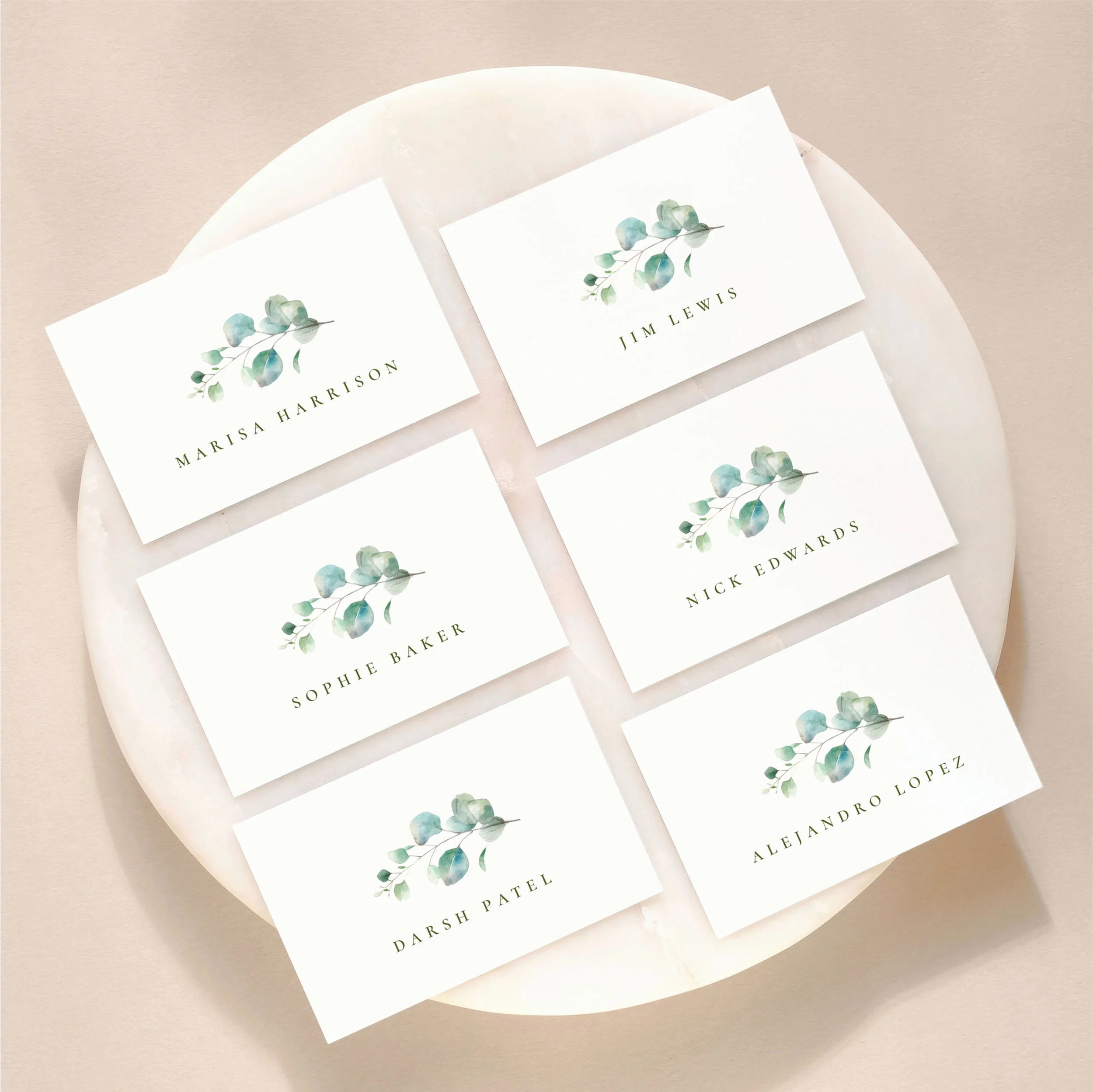 A set of 6 small, flat wedding place cards on a marble tile with printed guest names and a eucalyptus leaf illustration