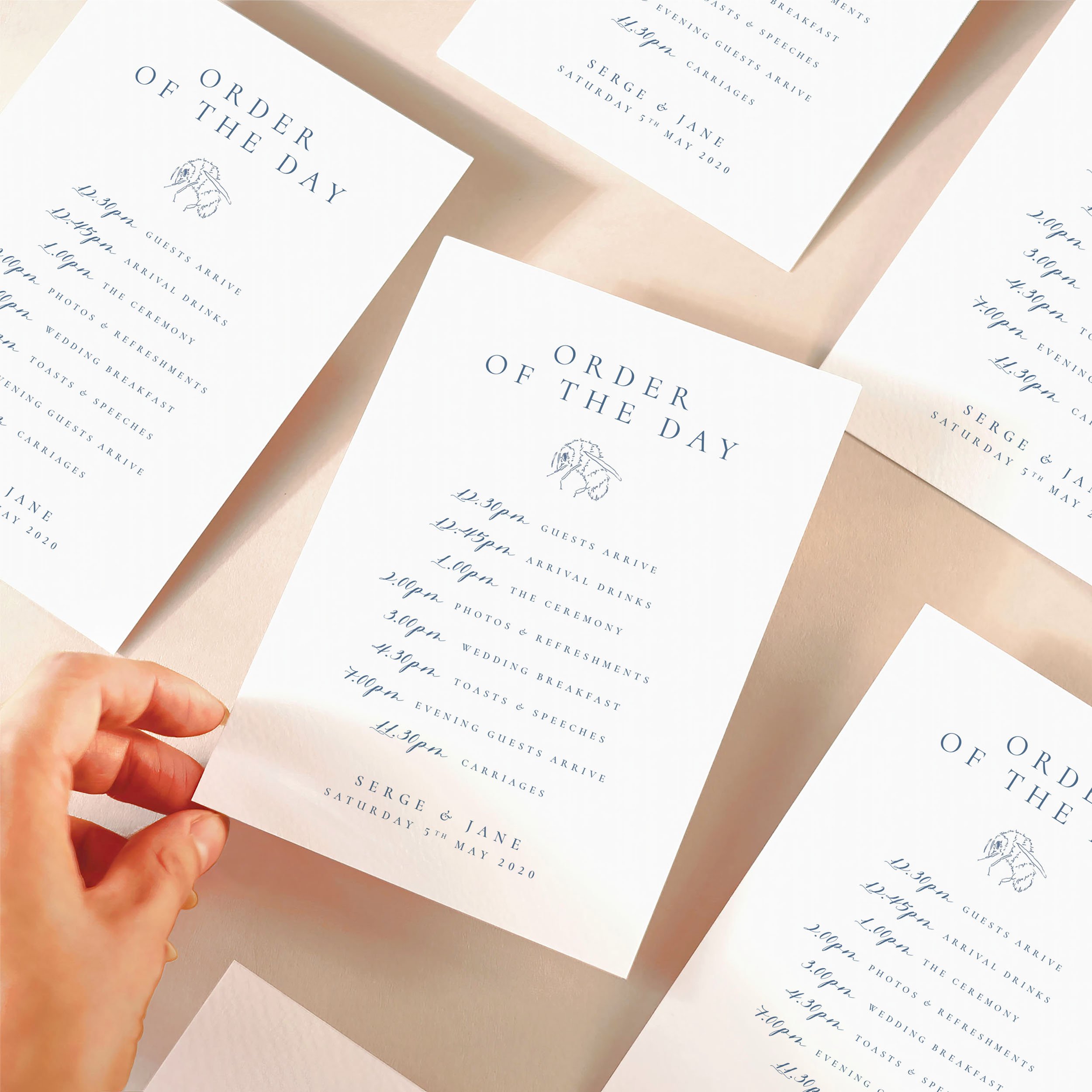 A hand picking up an order of the day timeline card with a dusty blue design featuring a bumble bee