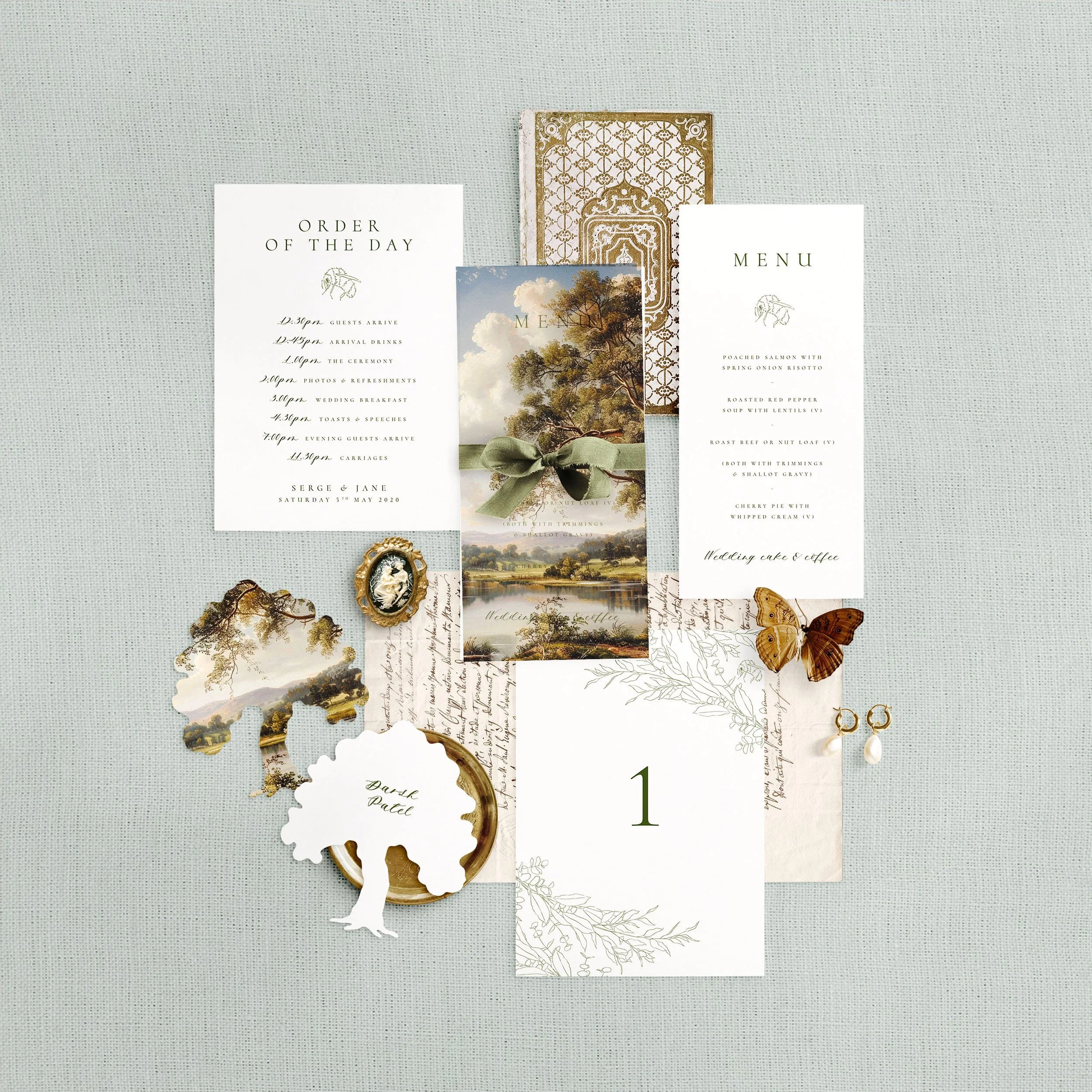 Wedding stationery flat lay featuring a menu, table number, order of the day and a tree shaped place card. Each has a delicate green floral design with a bumble bee.