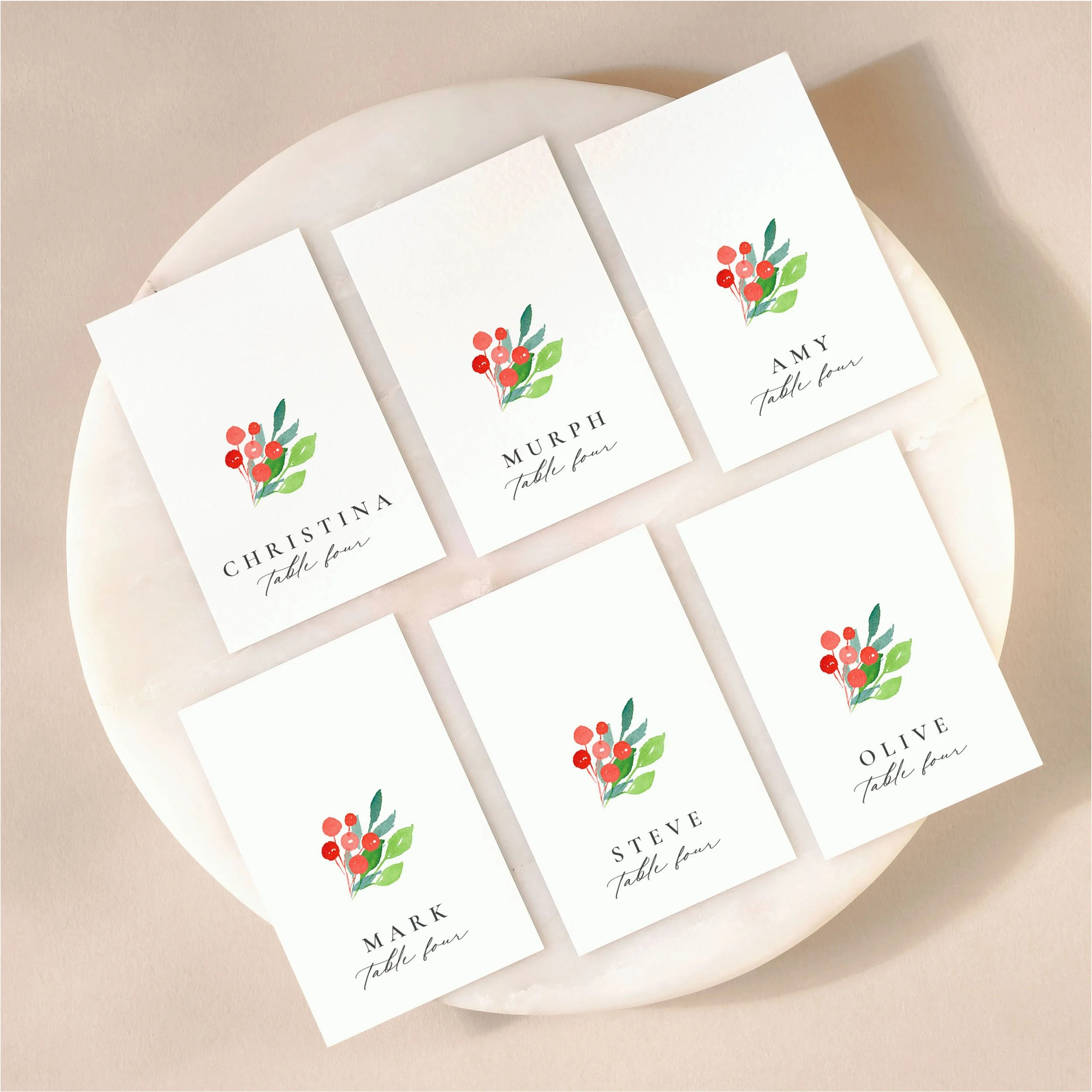 A set of 6 small, flat wedding place cards on a marble tile with printed guest names and watercolour red berries.