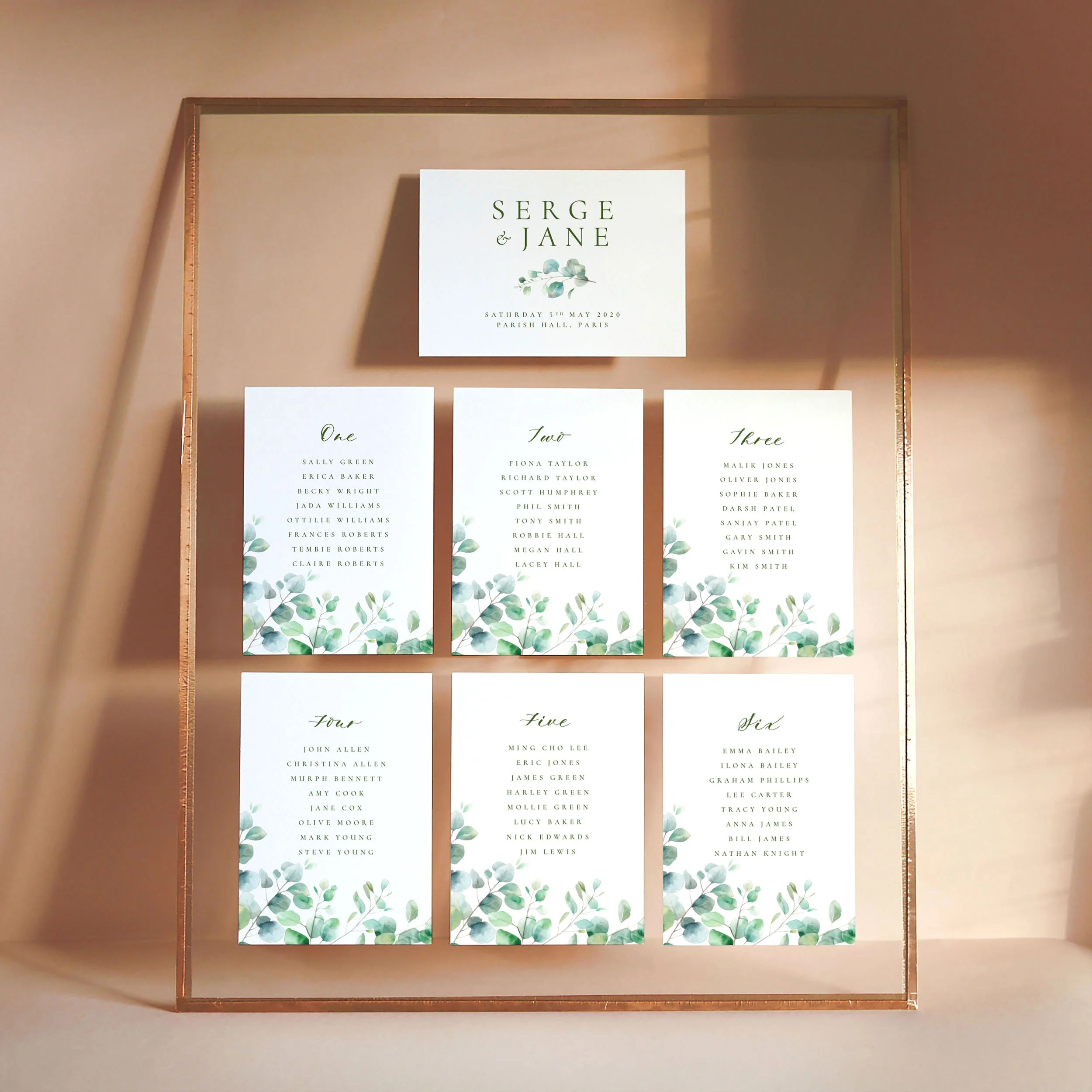 A set of printed table plan cards in a glass frame with copper edges. The design has watercolour eucalyptus leaves.