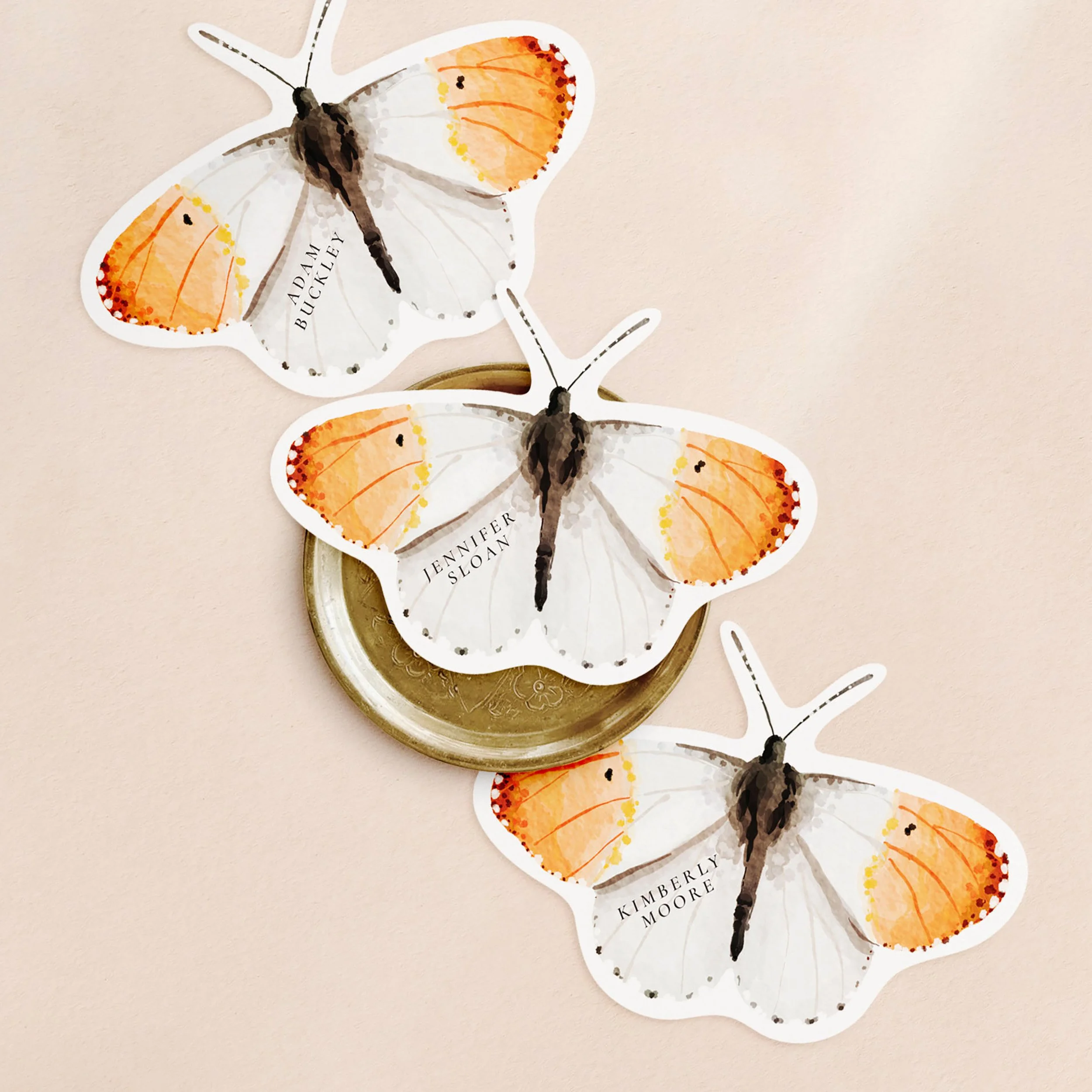 Three butterfly-shaped place cards with an orange-tip butterfly watercolour painting on one side and a different guest name printed on each.