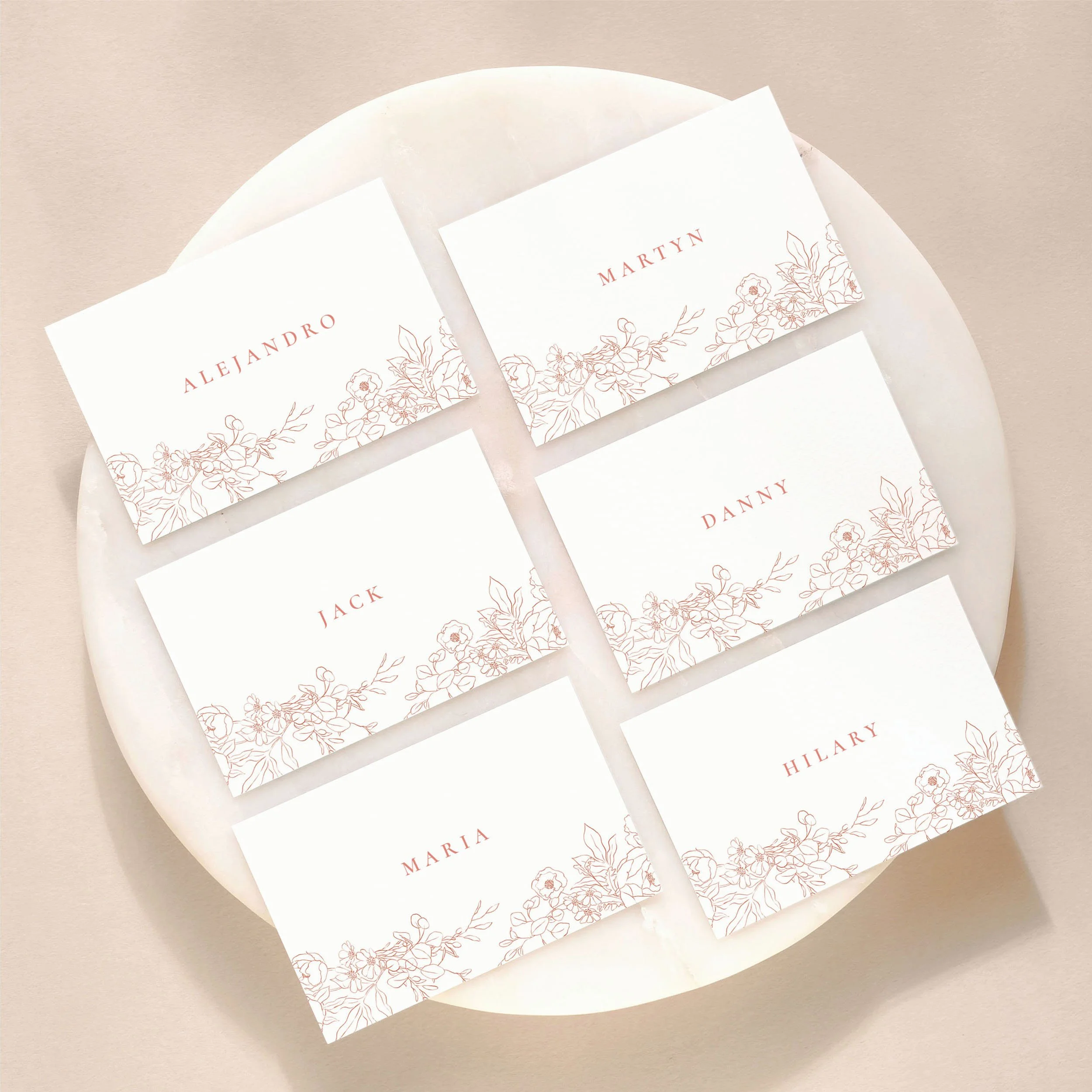 A set of 6 small, flat wedding place cards on a marble tile with printed guest names and illustrated pink floral imagery.