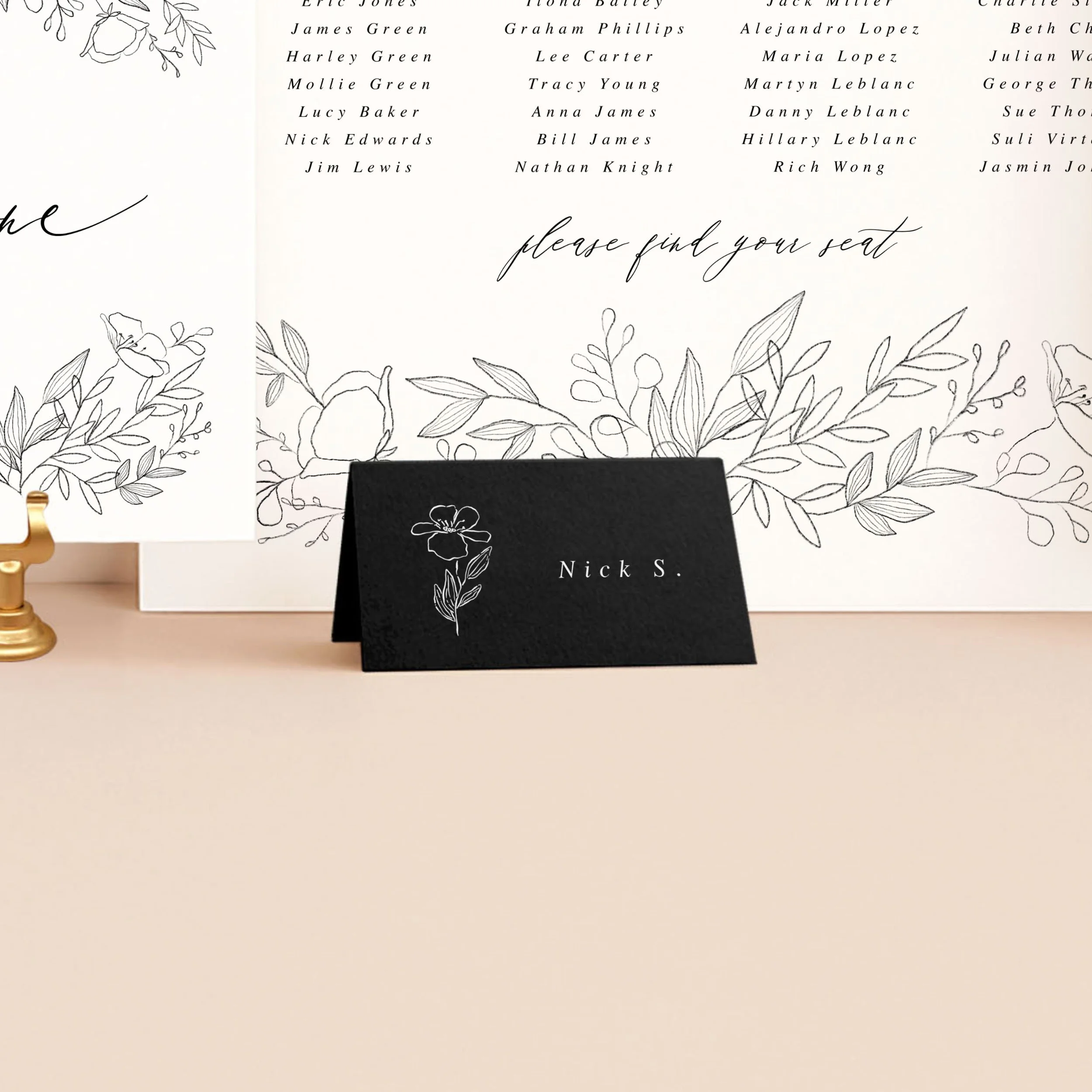 A modern black tent place card, printed in white ink with a guest name and a small flower illustration.