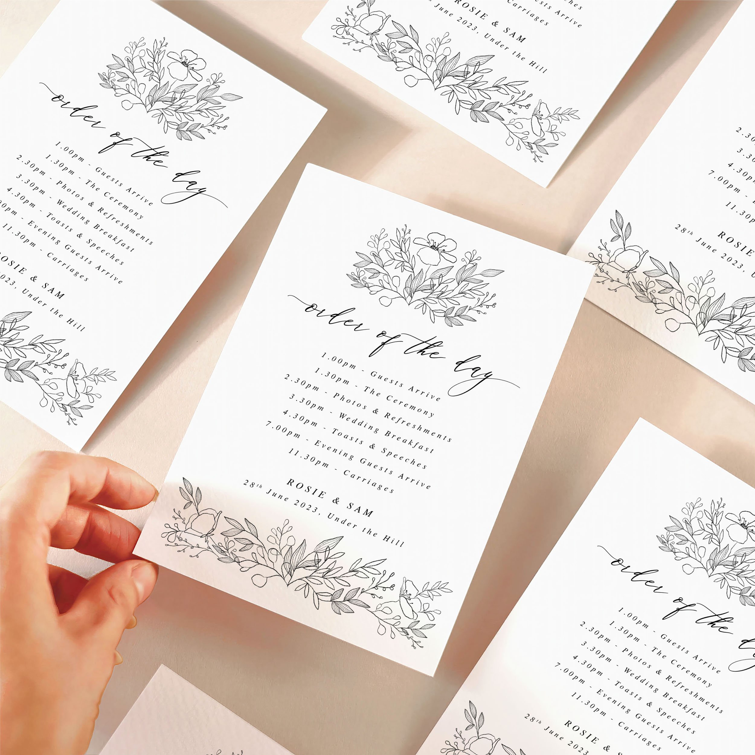 A hand picking up an order of the day timeline card with a black floral motif design