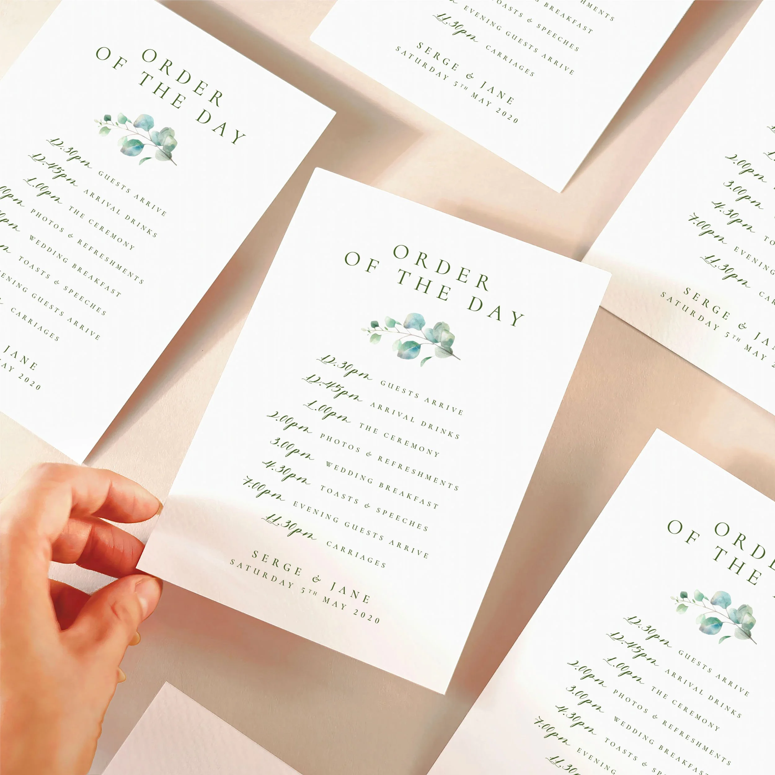 A hand picking up an order of the day timeline card with a eucalyptus leaf design