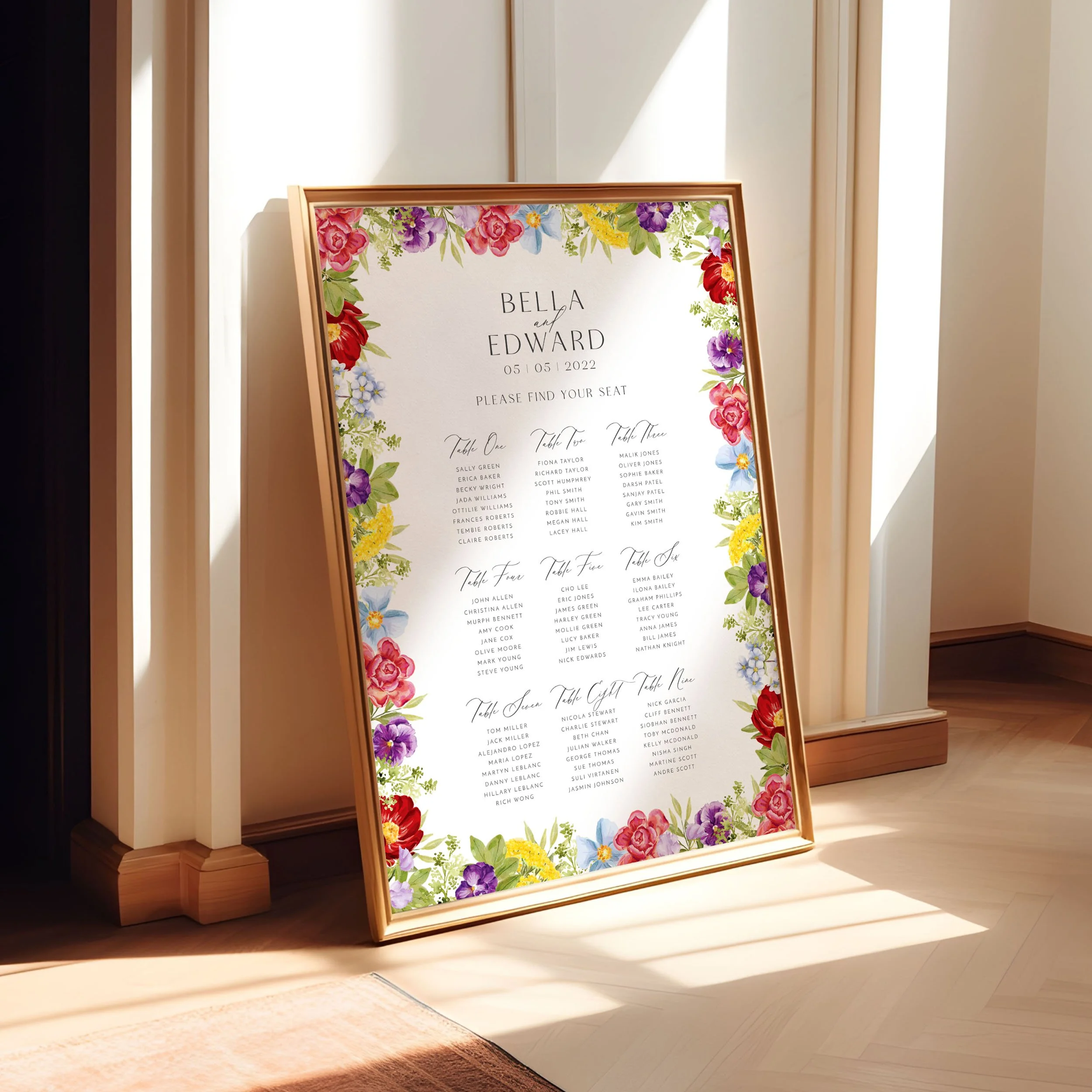 A framed A1 table plan sign leaning against a wall as the light spills across. The design has colourful hand-painted flowers around the edges.