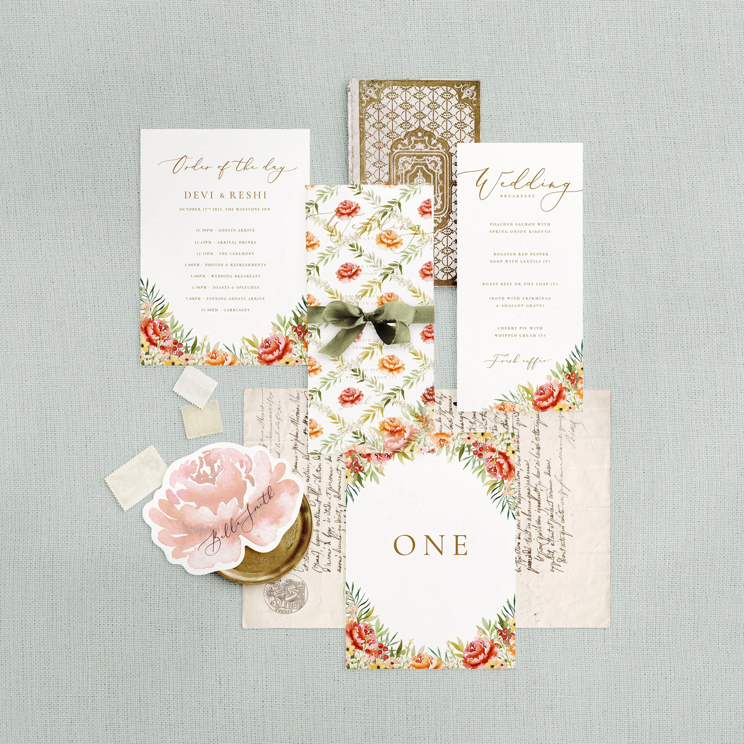 Wedding stationery flat lay featuring a menu, table number, order of the day and a flower shaped place card. A burnt orange watercolour floral design.