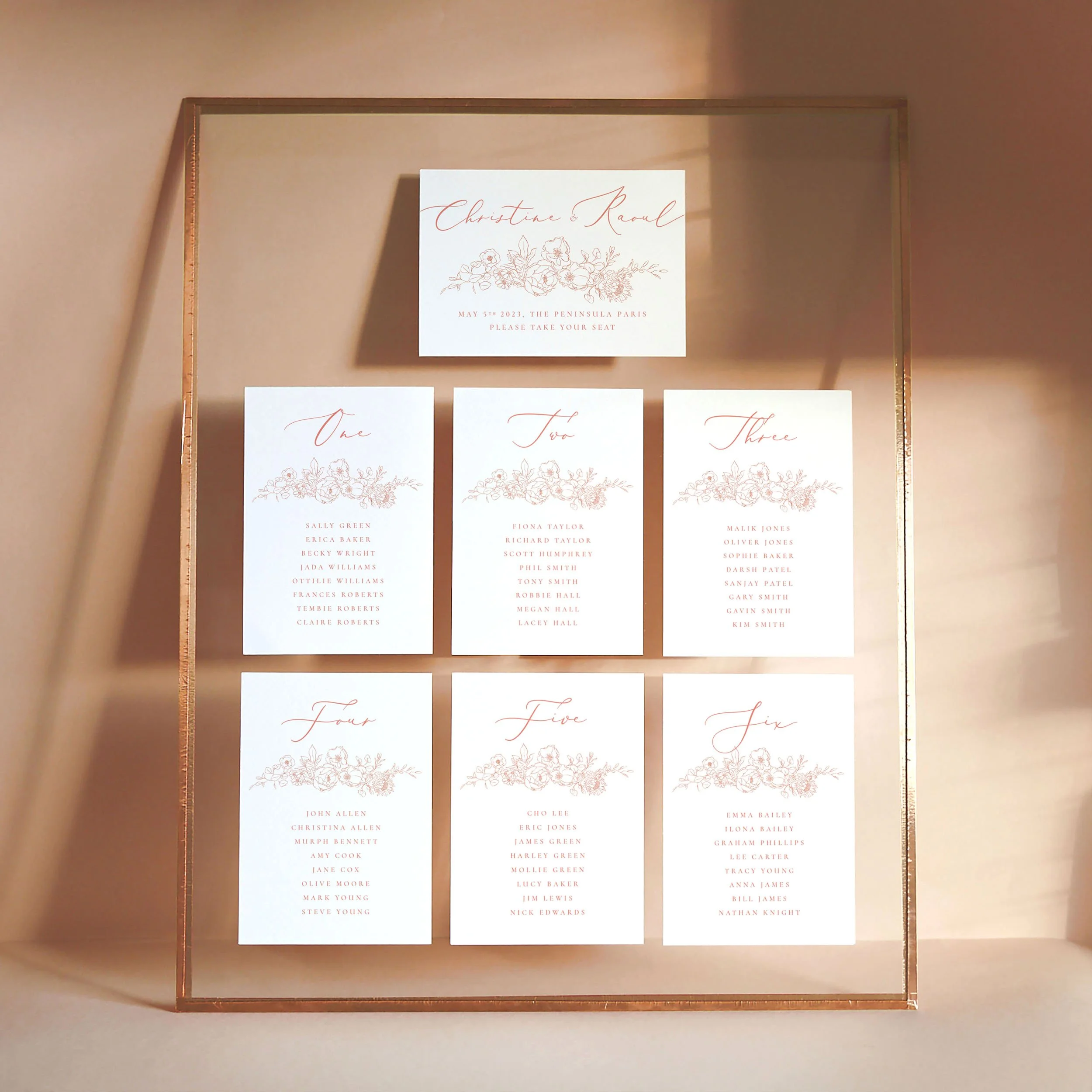 A set of small A6 printed table plan cards in a glass frame with copper edges. The design has illustrated flowers and leaves spilling down the right-hand side.